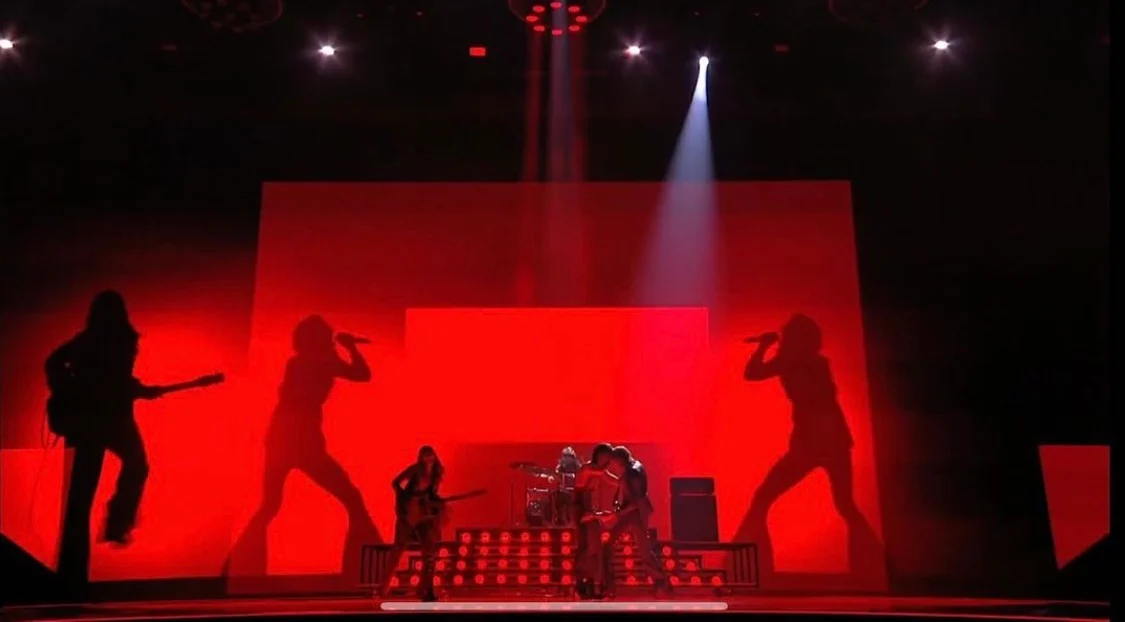 Palco immerso nella luce rossa, con sagome nere della band proiettate sui fondali – Måneskin all'Eurovision 2021, Rotterdam, Paesi Bassi – scenografia per concerti