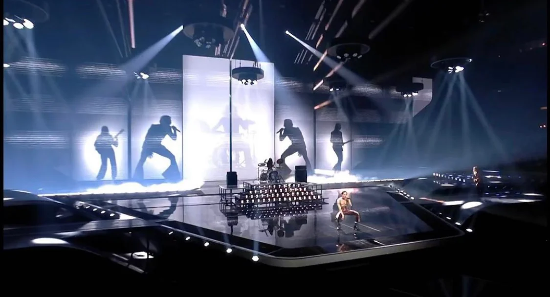 Vista d'insieme del palco dell'Eurovision 2021: enormi sagome della band su fondali bianchi, fasci di luce e pavimento a specchio – Måneskin all'Eurovision 2021, Rotterdam, Paesi Bassi – scenografia per concerti