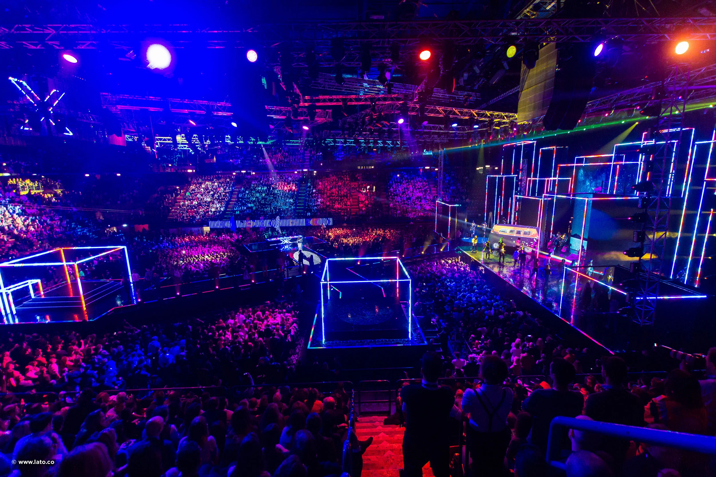Vista d'insieme della finale di X Factor al Forum di Milano, con palchi a cubo profilati al neon e l'arena gremita – Finale di X Factor 2016, Milano, Italia – scenografia televisiva