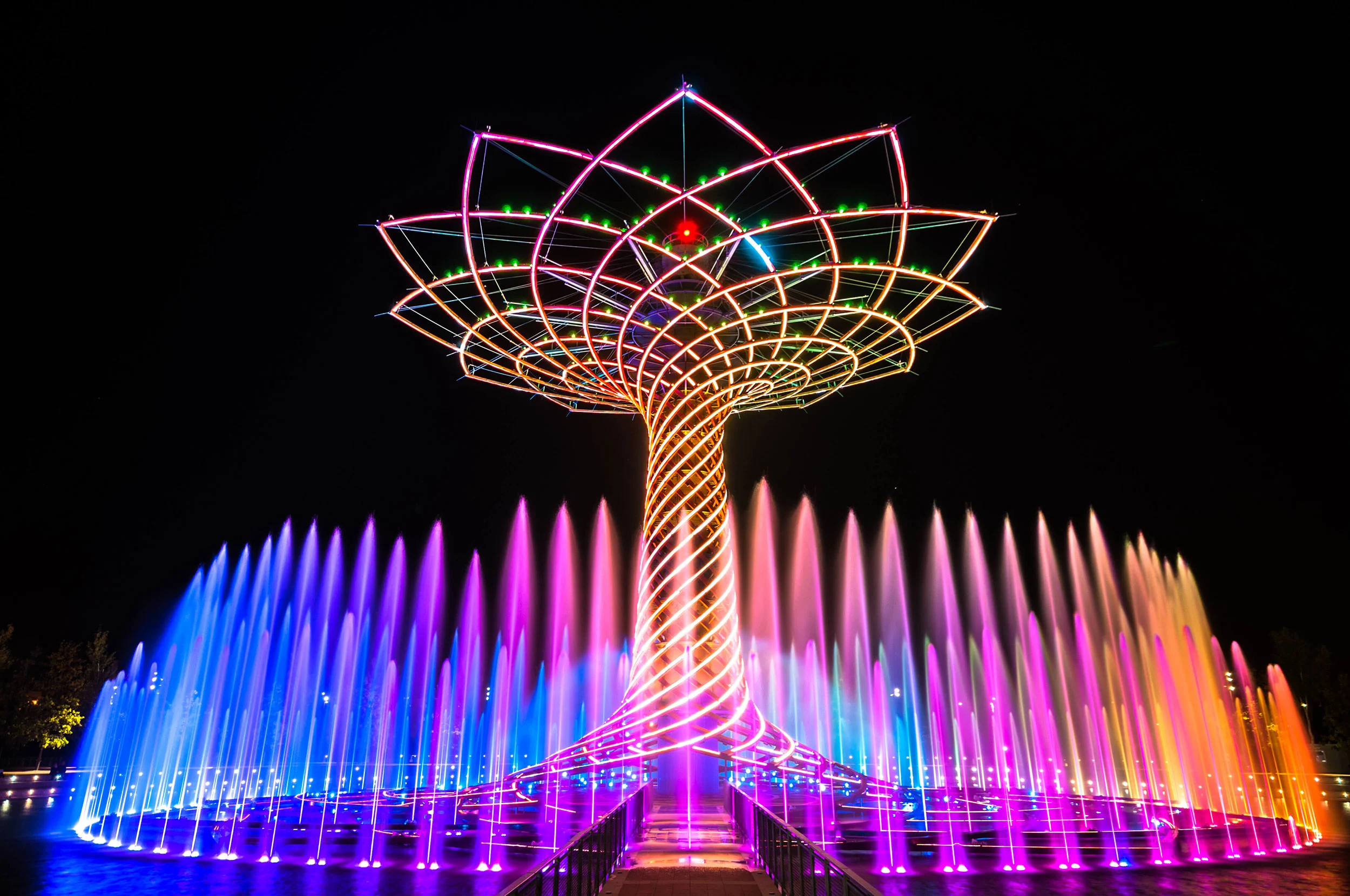 Albero della Vita illuminato di rosa, arancione e viola, con getti della fontana multicolori intorno – Albero della Vita all'Expo 2015, Milano, Italia – progettazione di installazioni
