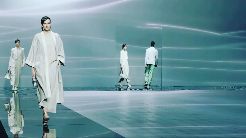 Modelle che sfilano su un pavimento a specchio davanti a pareti grigio-verdi chiare con tenui scie di luce – Giorgio Armani SS21 Donna, Milano, Italia, 2021 – scenografia per sfilate