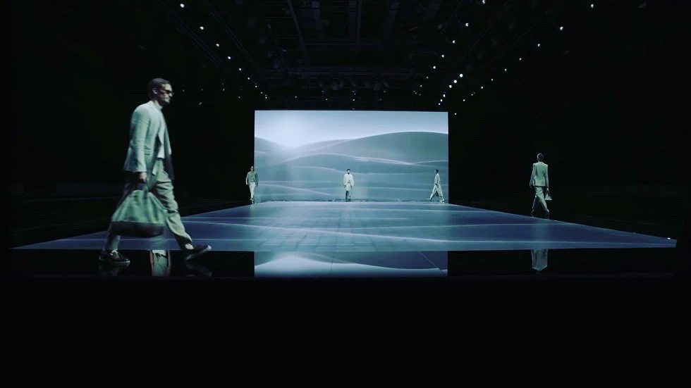 Modelle che attraversano una passerella a specchio davanti a una parete LED con dune chiare e ondulate – Giorgio Armani SS21 Donna, Milano, Italia, 2021 – scenografia per sfilate