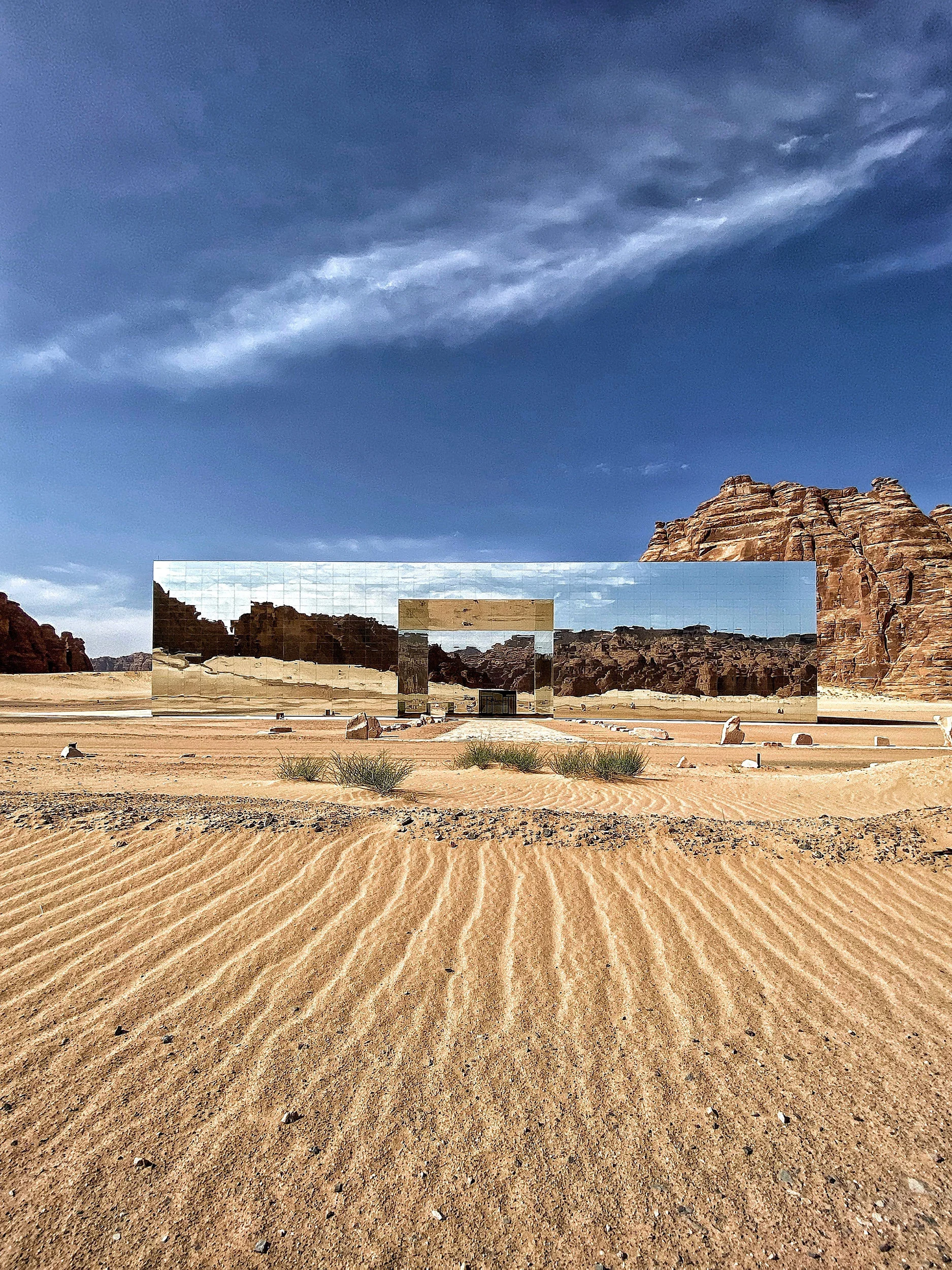 Facciata a specchio vista oltre dune di sabbia increspate, che riflette deserto e rocce sotto un cielo azzurro – Maraya Concert Hall, AlUla, Arabia Saudita, 2019 – architettura
