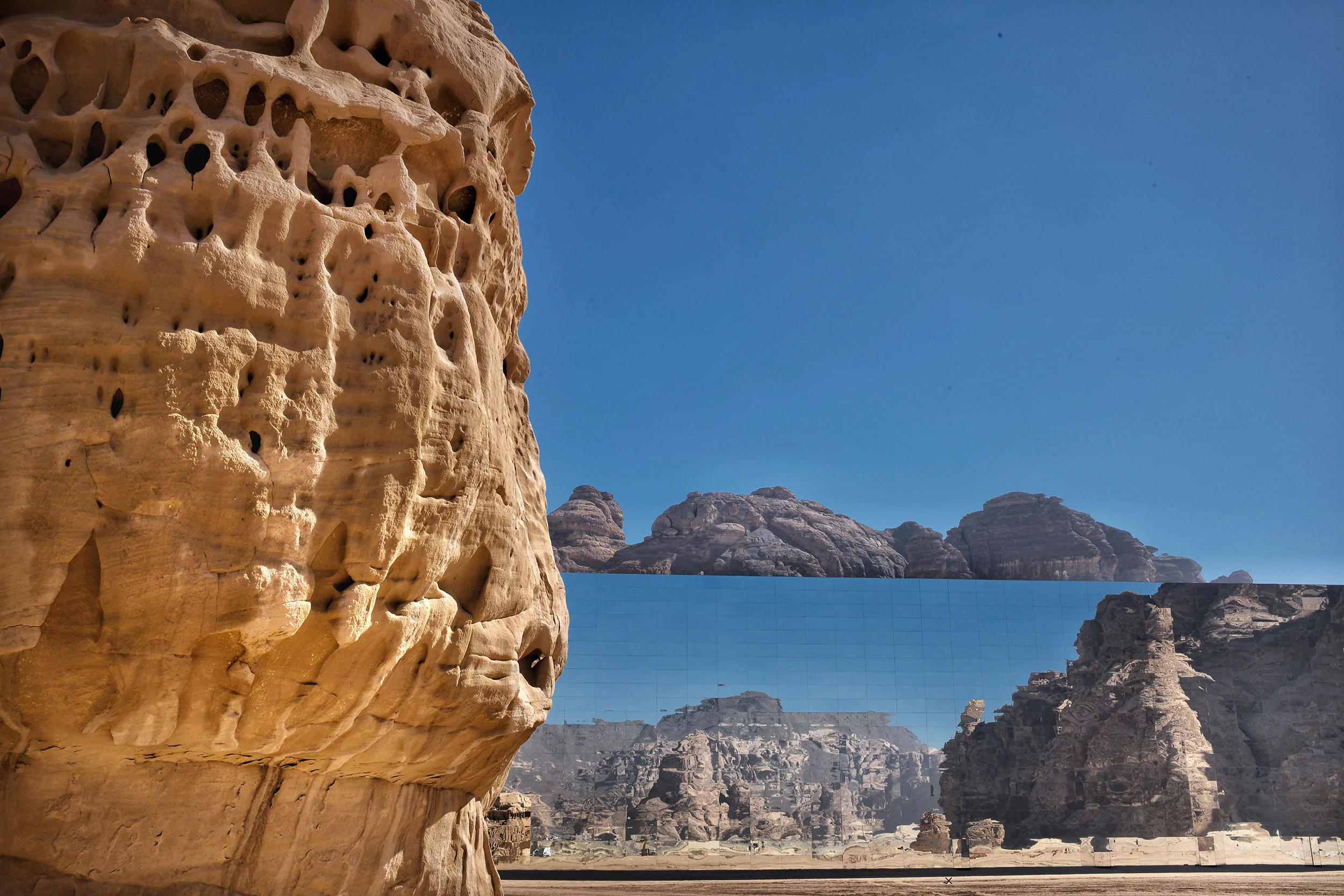 Roccia di arenaria erosa in primo piano e la facciata a specchio che riflette le falesie alle spalle – Maraya Concert Hall, AlUla, Arabia Saudita, 2019 – architettura