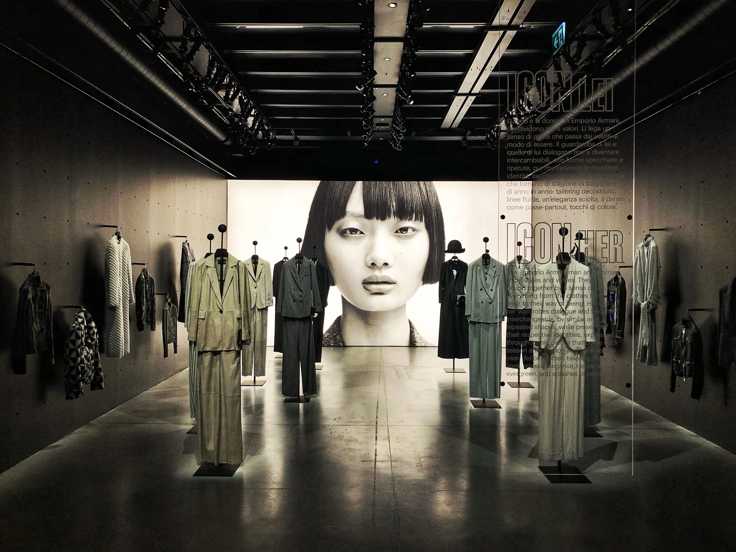 Sala di abiti su supporti che conduce a un grande ritratto in bianco e nero, con un testo su un pannello di vetro – Emporio Armani The Way We Are, Milano, Italia, 2020 – allestimento espositivo
