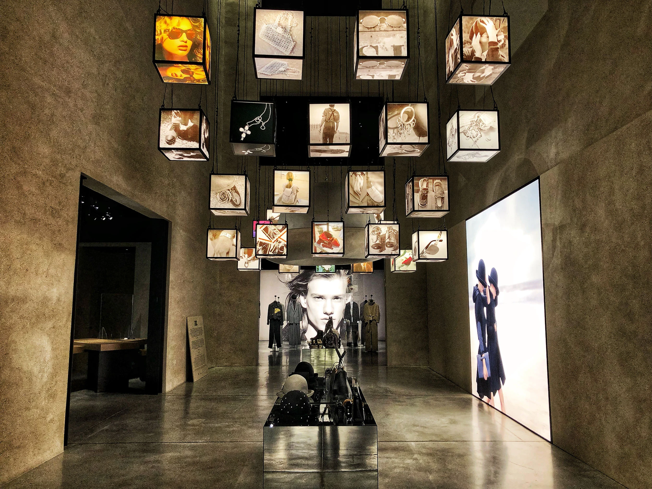 Sala espositiva con cubi luminosi di immagini di accessori appesi al soffitto, un lightbox a destra – Emporio Armani The Way We Are, Milano, Italia, 2020 – allestimento espositivo