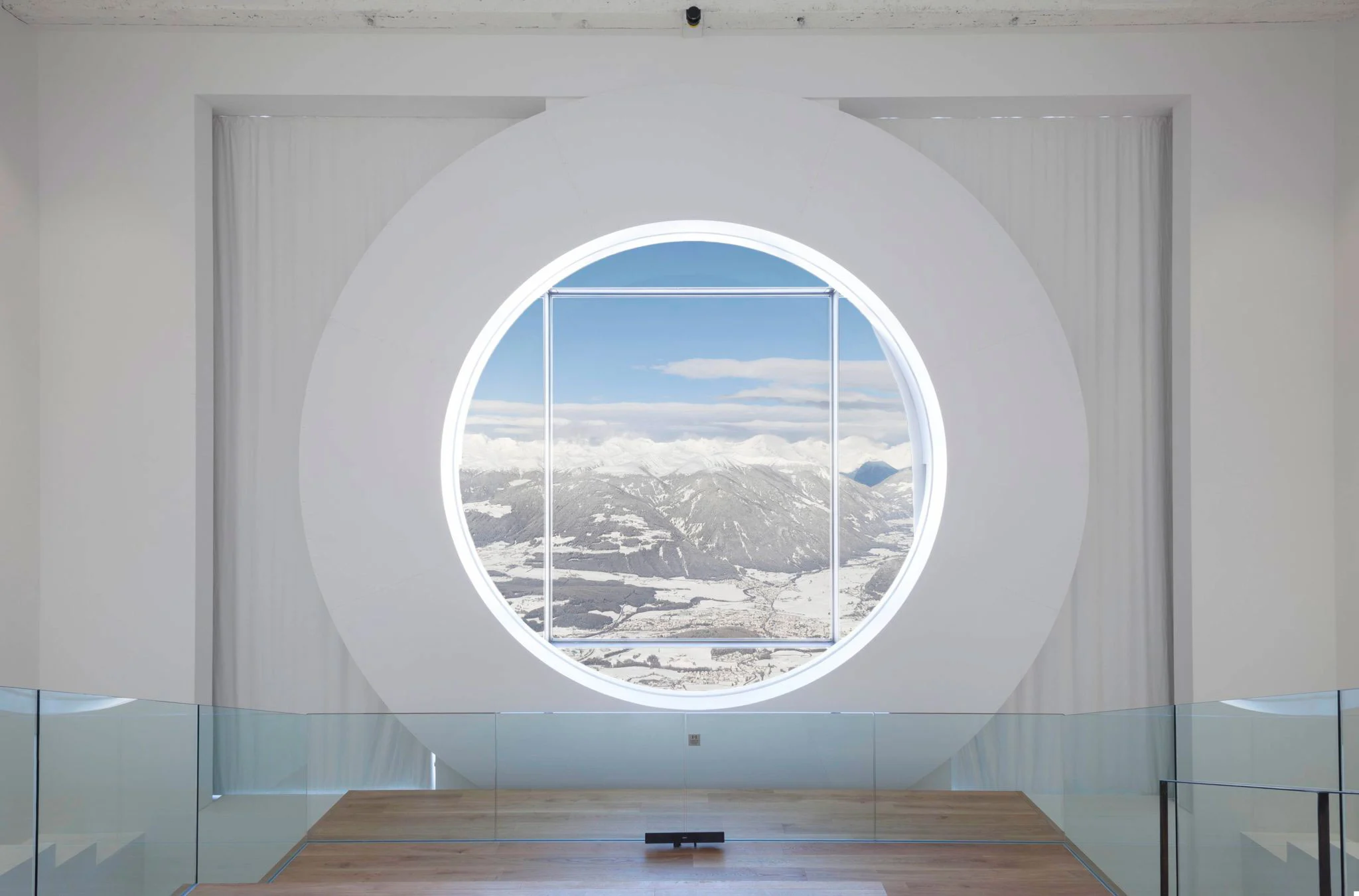 Grande finestra circolare in una parete bianca che inquadra un'ampia vista sulla valle innevata sottostante – Lumen Museo della fotografia di montagna, Plan de Corones, Italia, 2018 – architettura