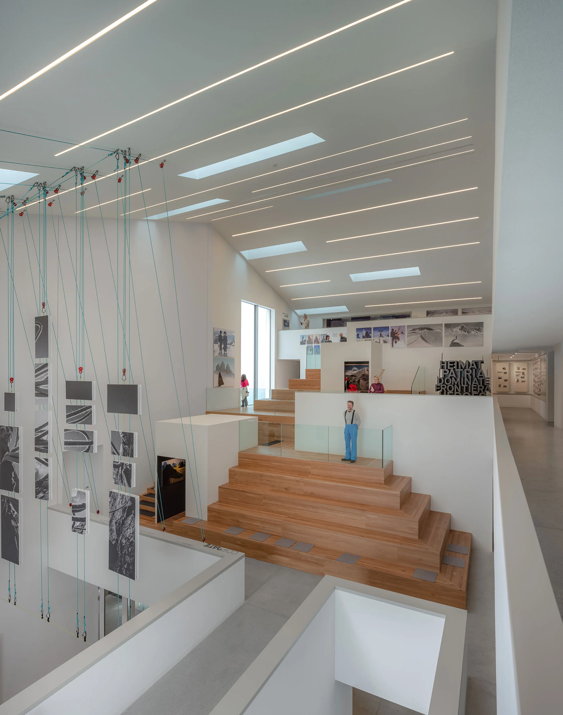 Interno del museo su più livelli con gradonate in legno, luci lineari a soffitto e fotografie appese a cavi – Lumen Museo della fotografia di montagna, Plan de Corones, Italia, 2018 – architettura