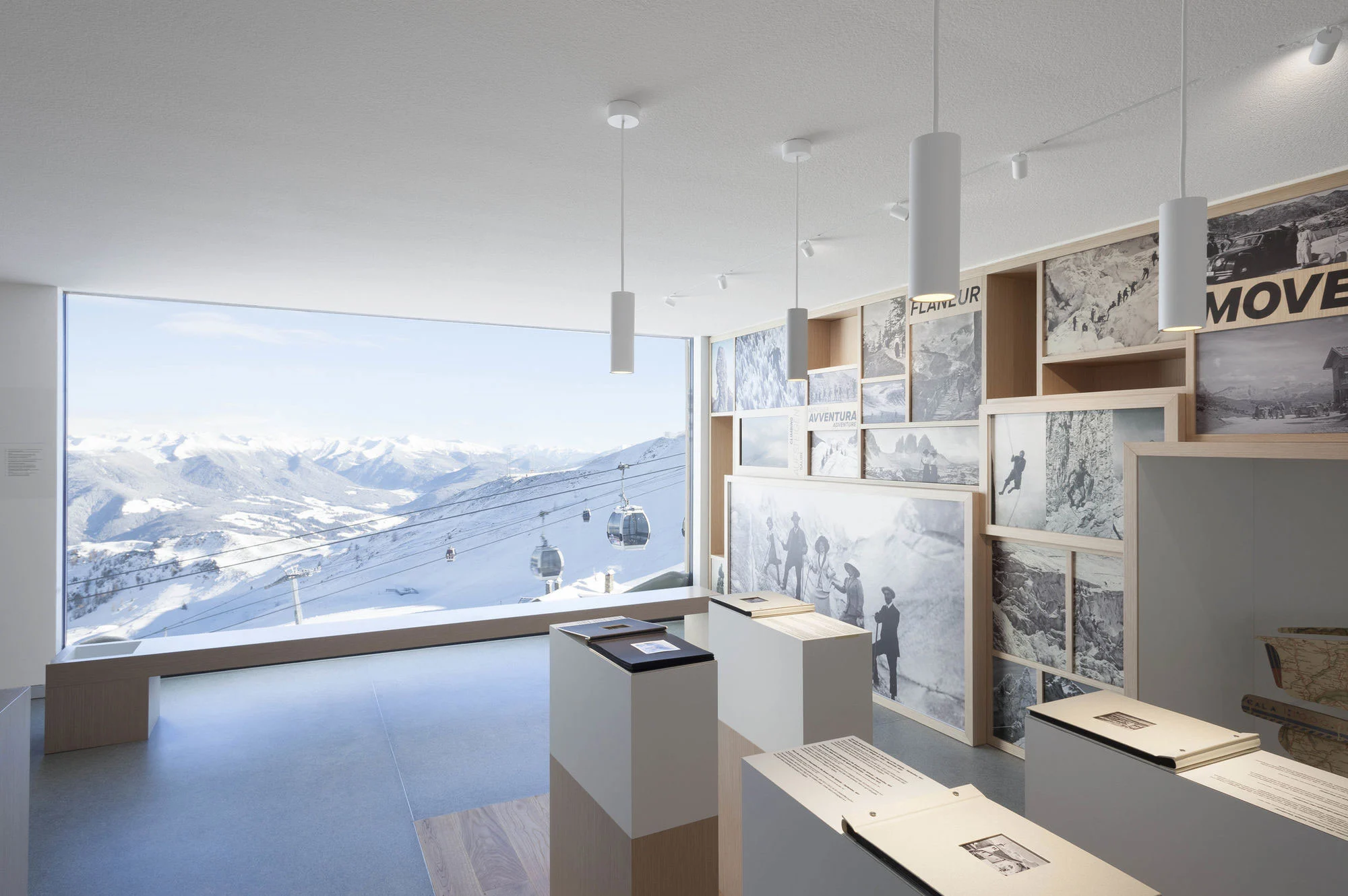 Sala espositiva con fotografie storiche di montagna ed espositori accanto a una vetrata panoramica su piste e funivie – Lumen Museo della fotografia di montagna, Plan de Corones, Italia, 2018 – architettura