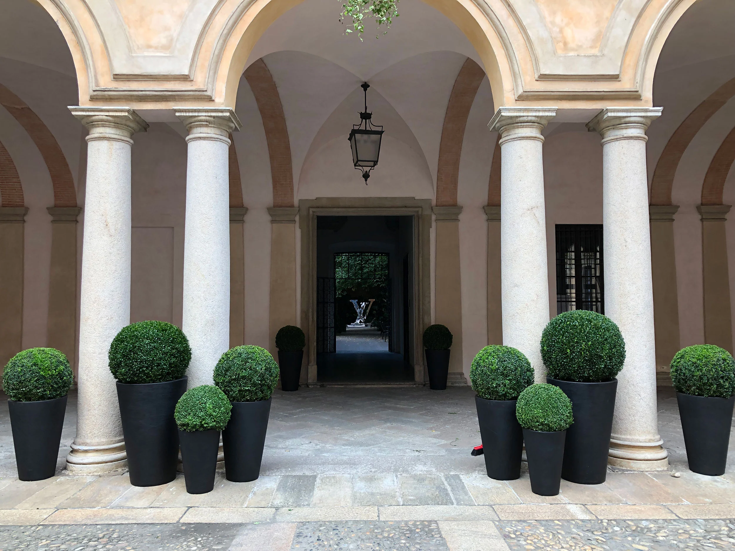 Colonnato con colonne in granito e vasi neri di sfere di bosso che inquadrano una porta sul giardino – Louis Vuitton a Palazzo Clerici, Milano, Italia, 2019 – allestimento espositivo