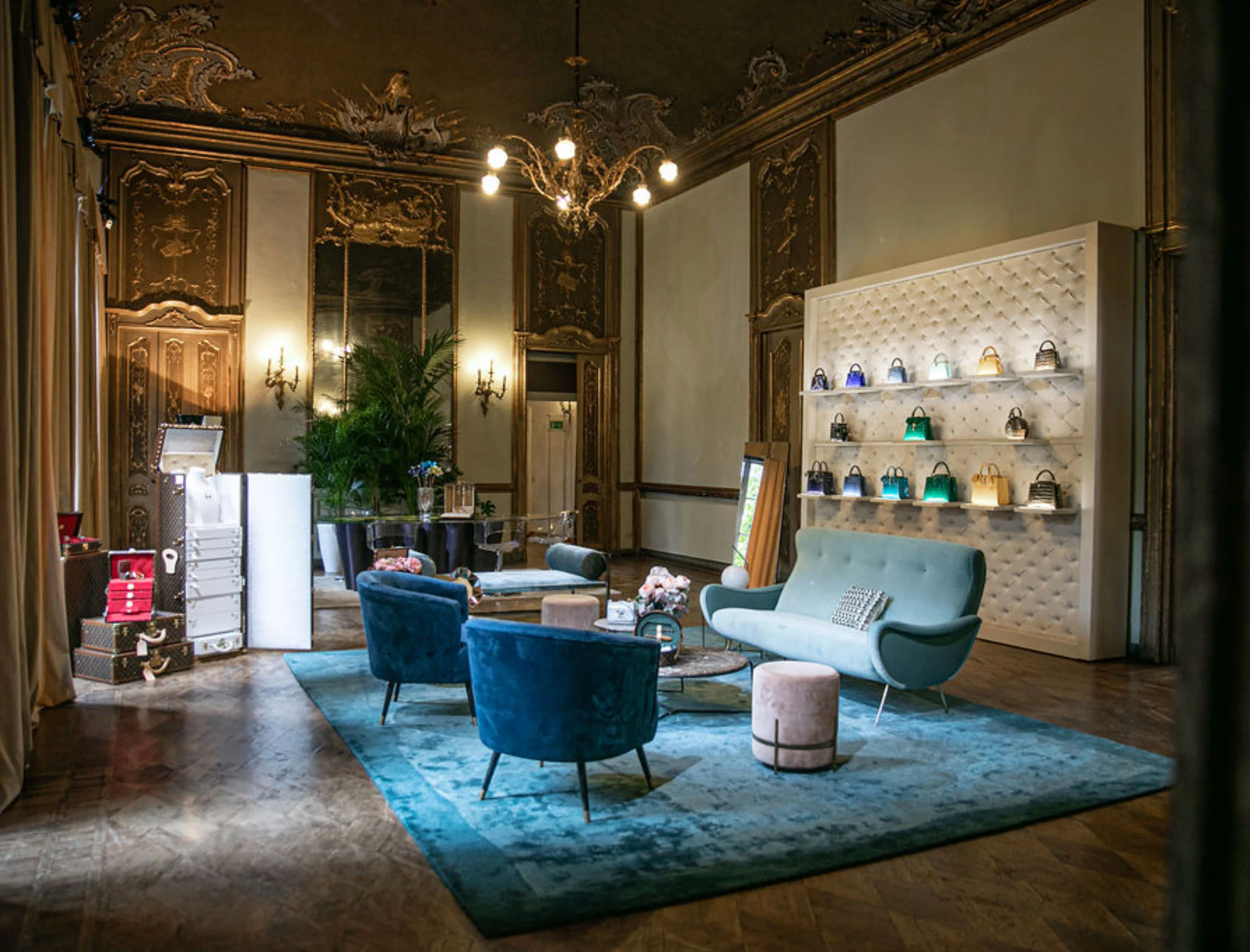Salone affrescato con sedie in velluto blu, un tappeto verde petrolio e una parete trapuntata che espone borse – Louis Vuitton a Palazzo Clerici, Milano, Italia, 2019 – allestimento espositivo
