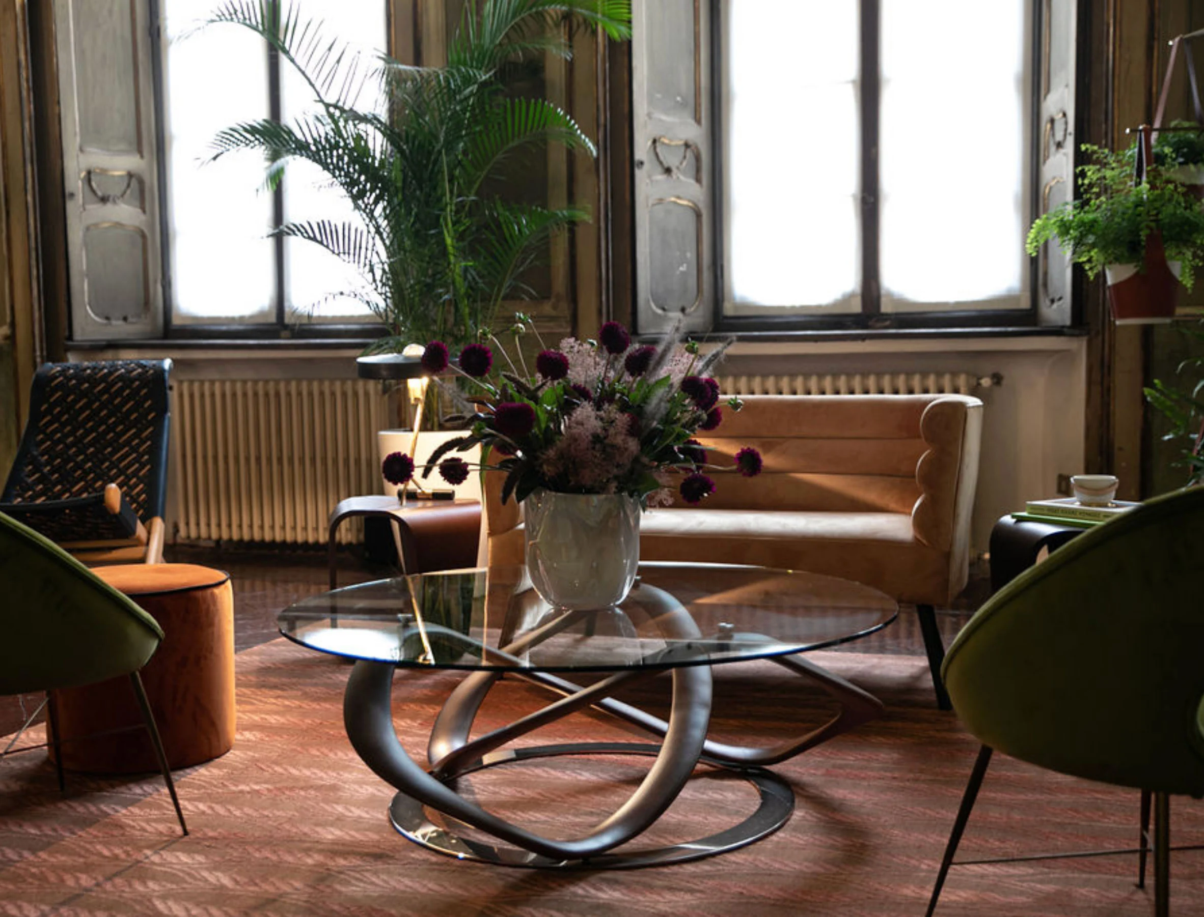 Angolo accanto ad alte finestre con un tavolo scultoreo in vetro, fiori viola e un divano in velluto ambra – Louis Vuitton a Palazzo Clerici, Milano, Italia, 2019 – allestimento espositivo