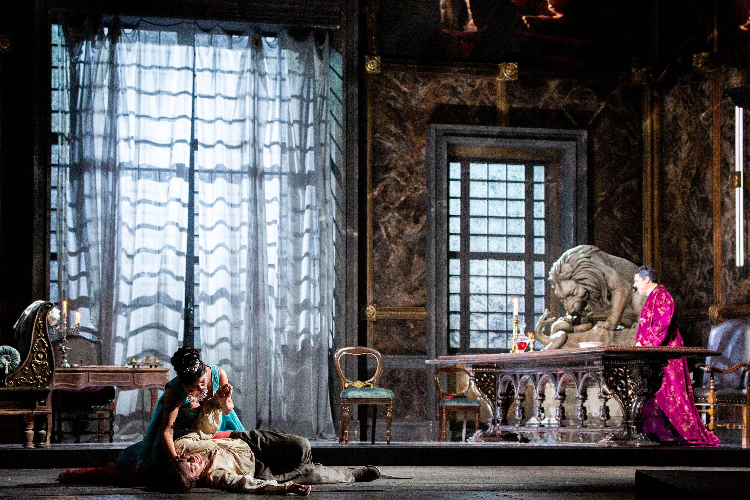 Tosca nel palazzo di Scarpia: una donna china su un uomo a terra, una scultura di leone e un'alta finestra con tende – Tosca al Teatro alla Scala, Milano, Italia, 2019 – scenografia d'opera
