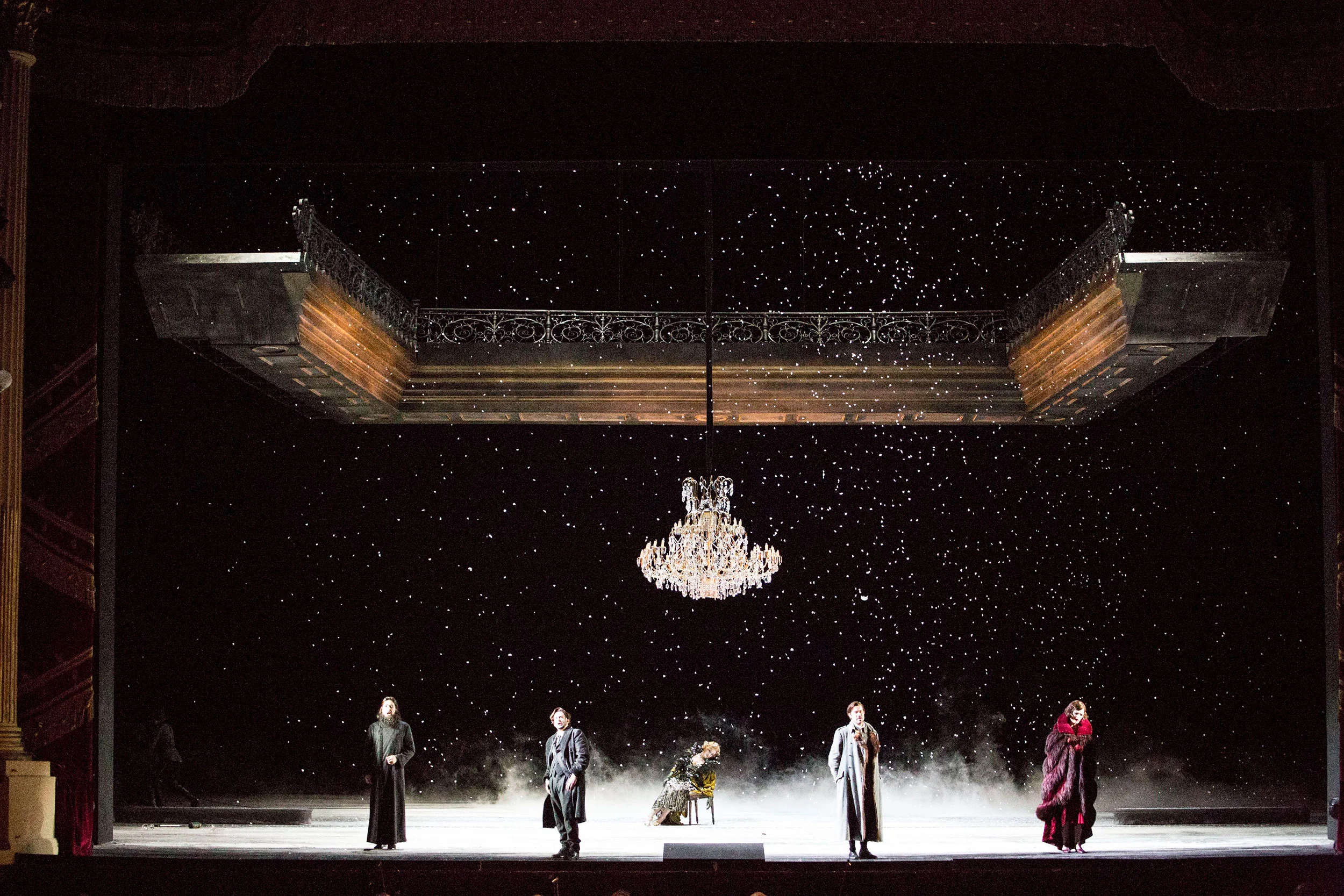 Neve che cade su un palco buio con un lampadario di cristallo e un balcone sospeso sopra cinque artisti – Tamerlano al Teatro alla Scala, Milano, Italia, 2017 – scenografia d'opera