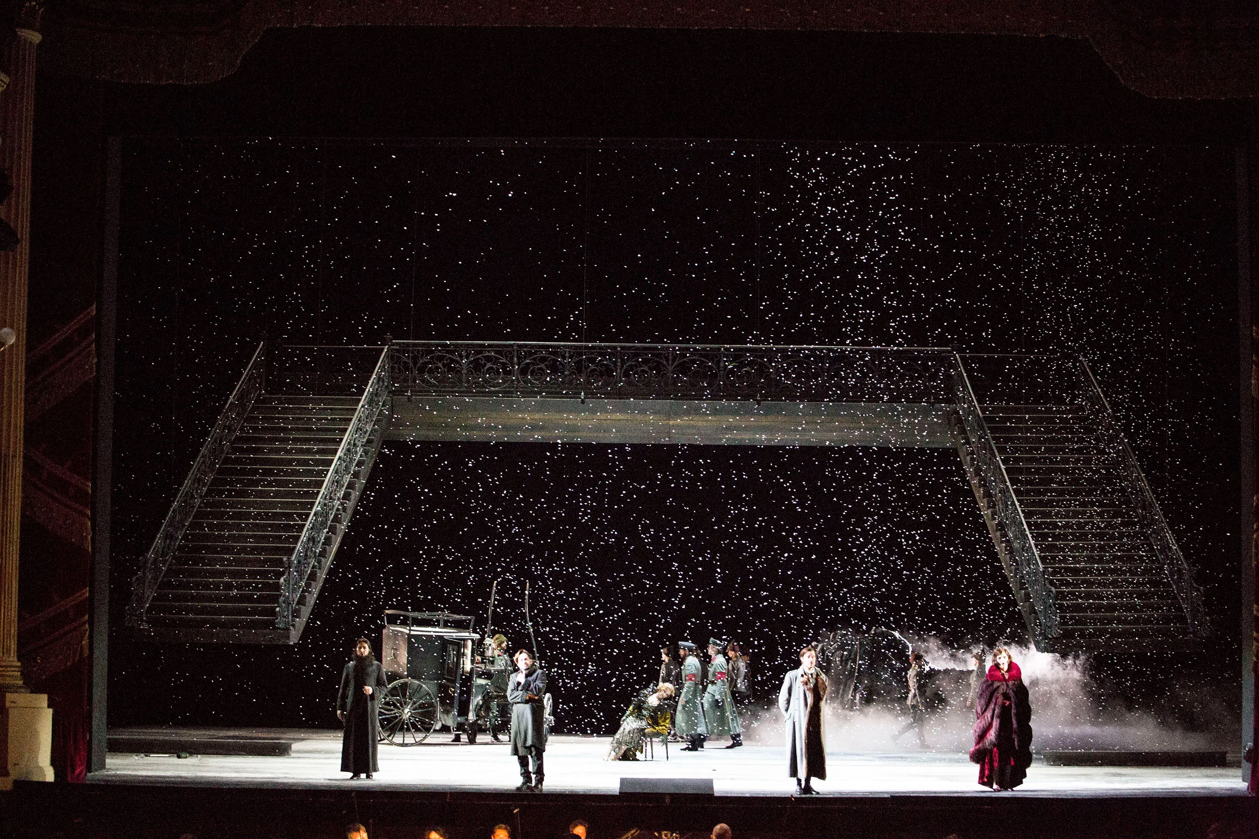 Vista d'insieme della scena innevata: doppia scalinata e ponte, carrozza e artisti sparsi sul palco – Tamerlano al Teatro alla Scala, Milano, Italia, 2017 – scenografia d'opera