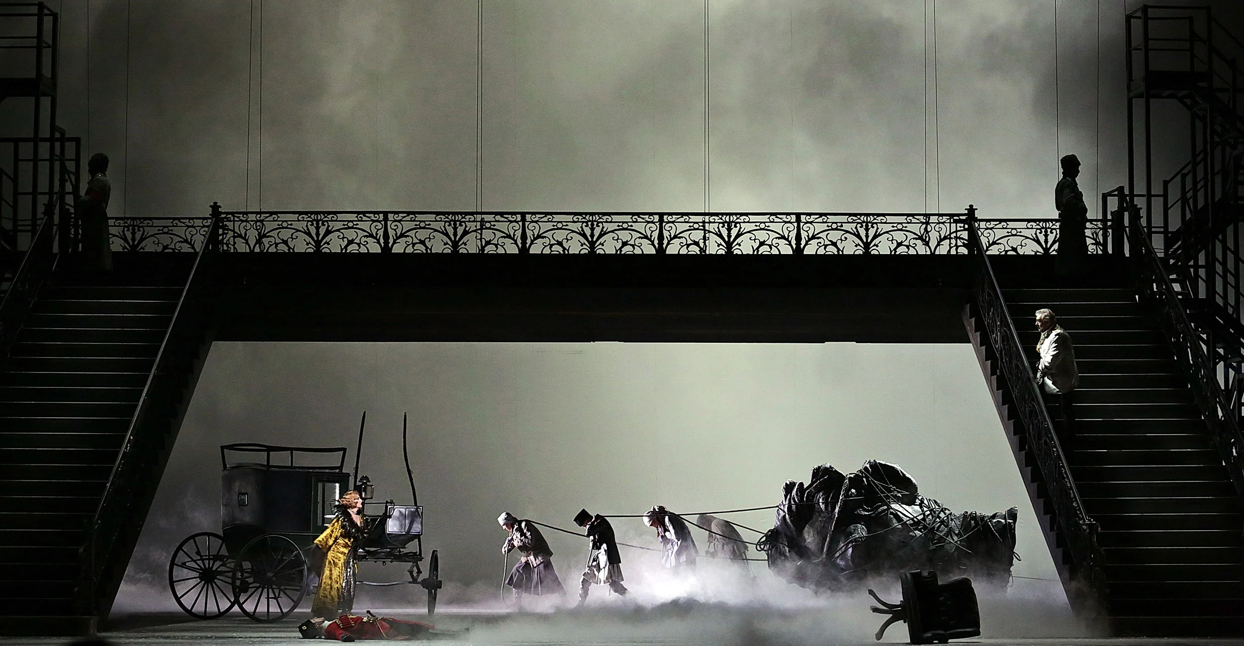 Ponte pedonale in ferro con scale sopra un palco nebbioso, figure che trascinano una carrozza e un cavallo caduto – Tamerlano al Teatro alla Scala, Milano, Italia, 2017 – scenografia d'opera