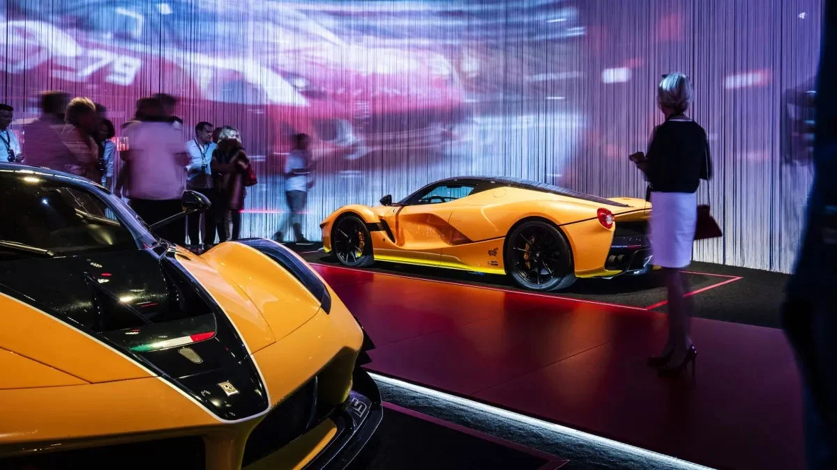 Supercar Ferrari gialle su una pedana illuminata di rosso davanti a una parete di tende a fili con video proiettati – Universo Ferrari alla Fabbrica del Vapore, Milano, Italia, 2019 – allestimento espositivo