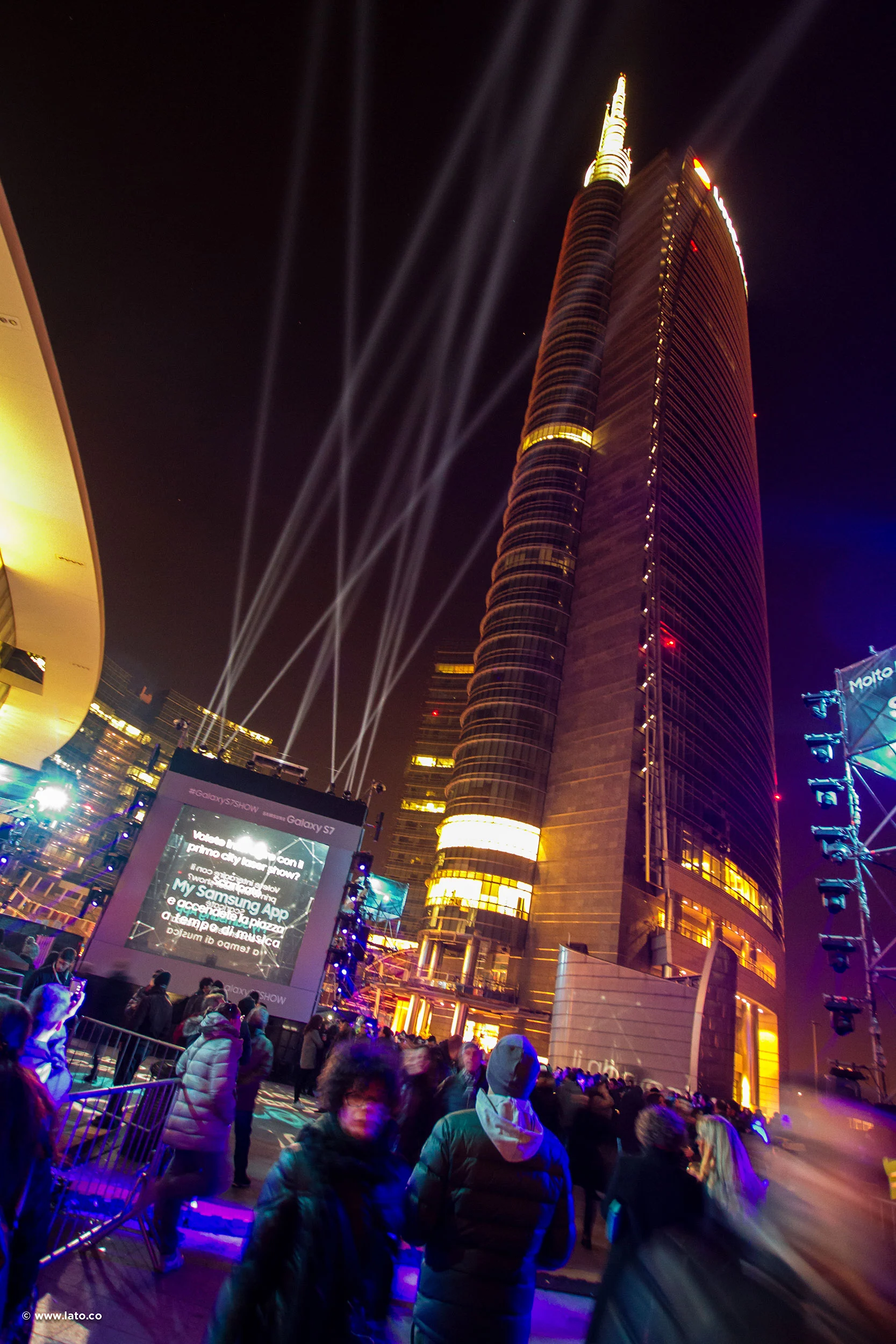 Vista notturna del grattacielo illuminato sopra Piazza Gae Aulenti, con fari e un grande schermo – Samsung Galaxy S7 Laser Show, Milano, Italia, 2016 – progettazione di eventi