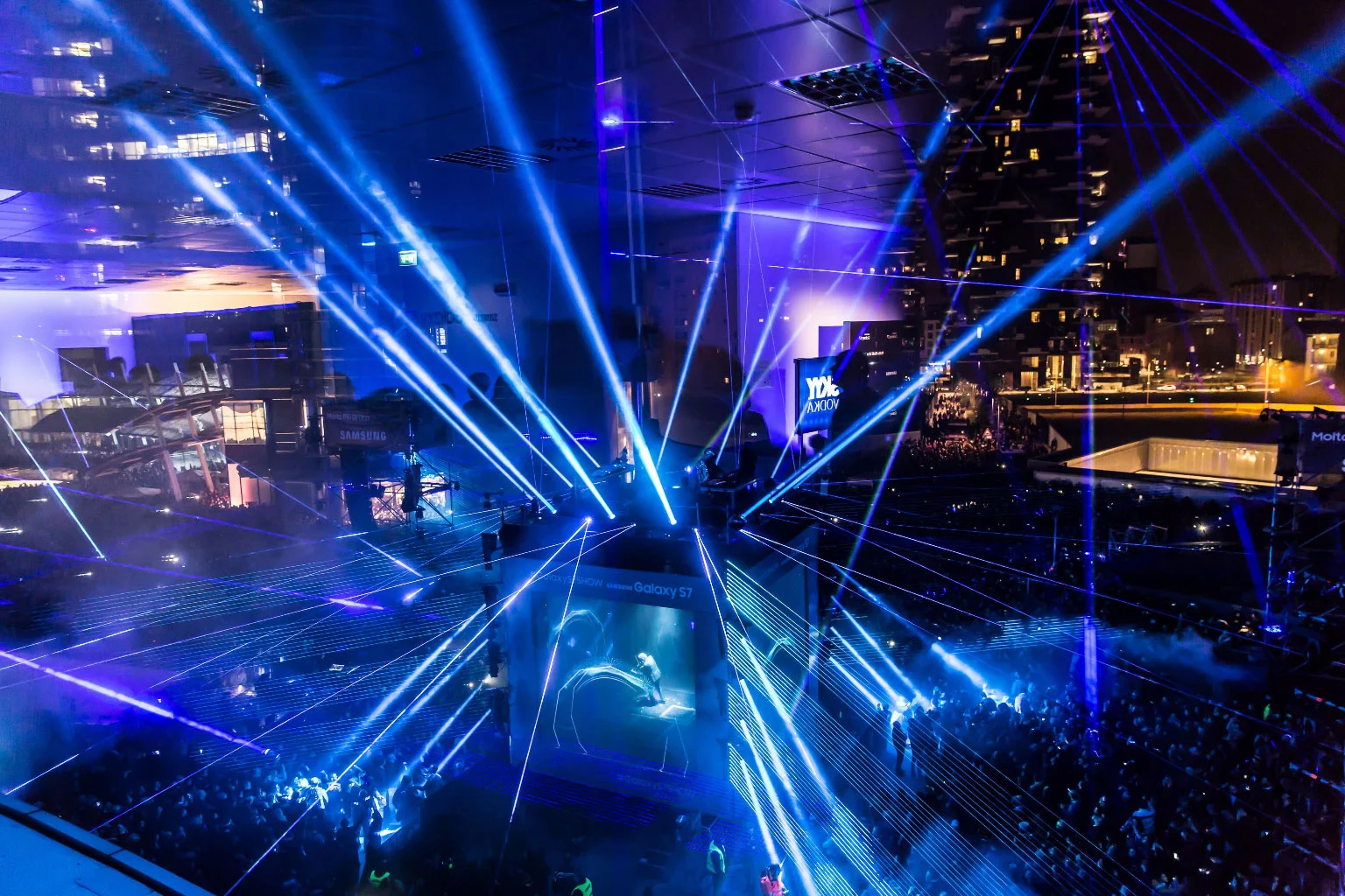 Vista aerea dello show laser per Samsung Galaxy S7: fasci laser blu incrociati sopra il pubblico e il palco – Samsung Galaxy S7 Laser Show, Milano, Italia, 2016 – progettazione di eventi