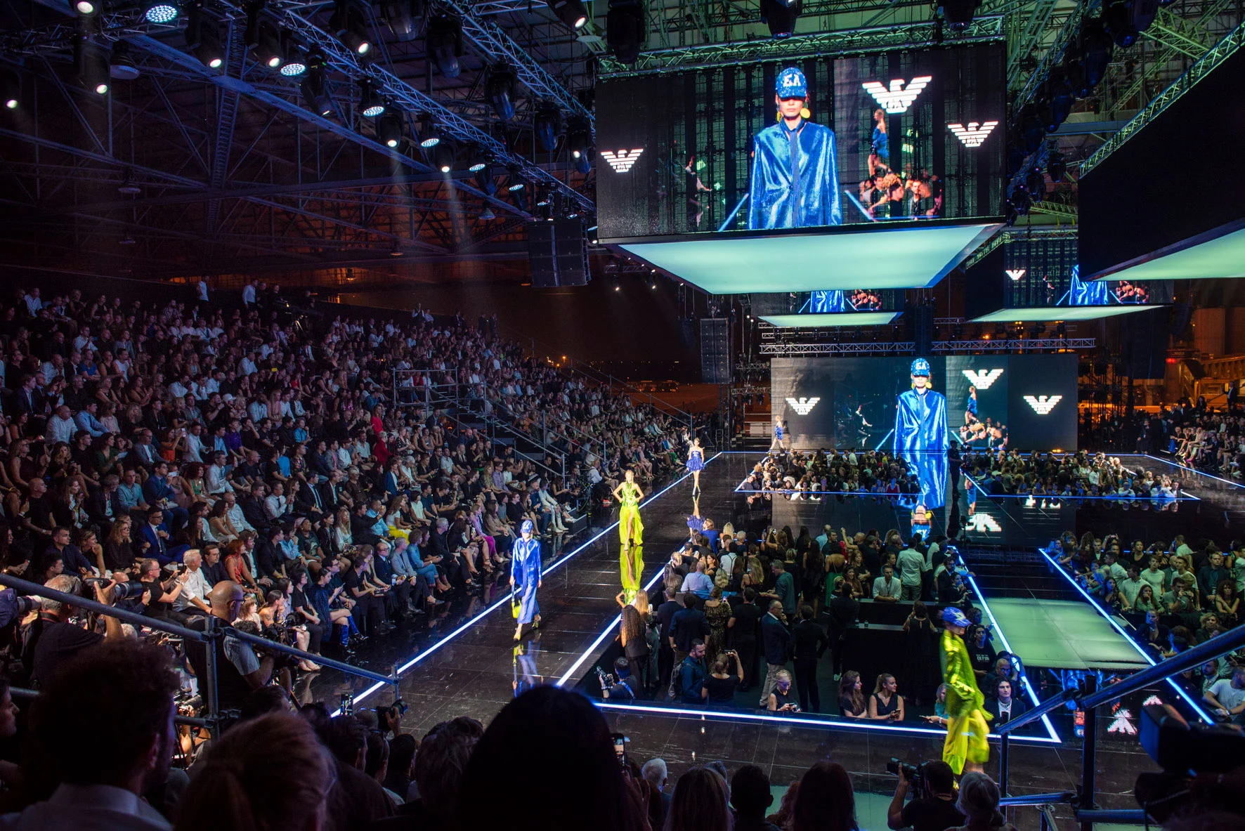 Sfilata Emporio Armani Boarding nell'hangar di Linate: modelli su passerelle illuminate sotto schermi video sospesi – Emporio Armani Boarding SS19, Milano, Italia, 2019 – scenografia per sfilate