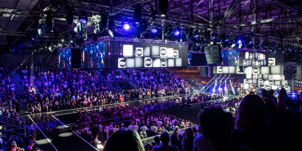 Hangar gremito di spettatori in luce blu, passerelle e schermi sospesi con i loghi RW – Emporio Armani Boarding SS19, Milano, Italia, 2019 – scenografia per sfilate