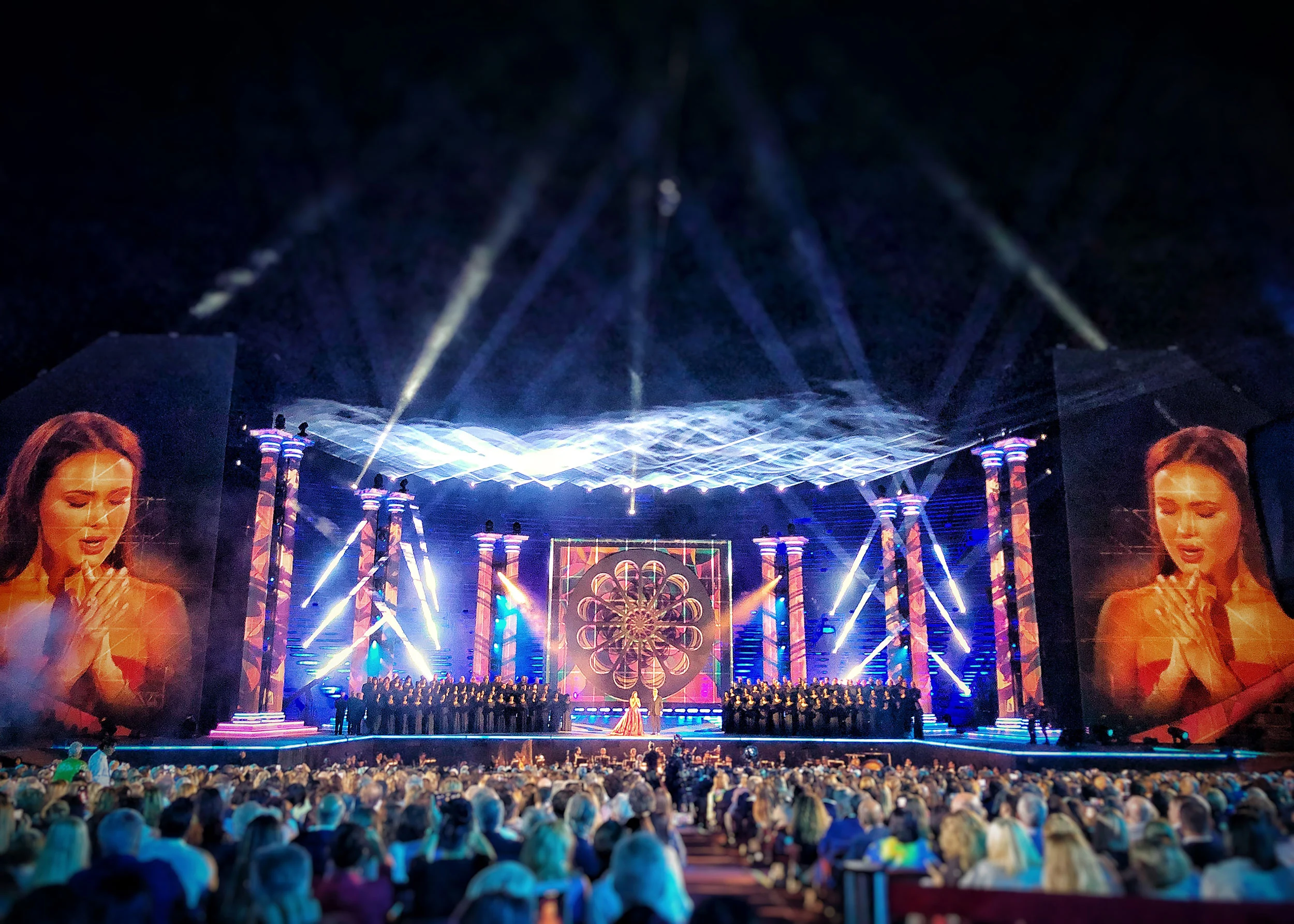 Coro sul palco tra colonne a strisce, un pannello a rosone al centro e un cantante sui giganteschi schermi laterali – La Notte di Andrea Bocelli all'Arena di Verona, Italia, 2018 – scenografia per concerti