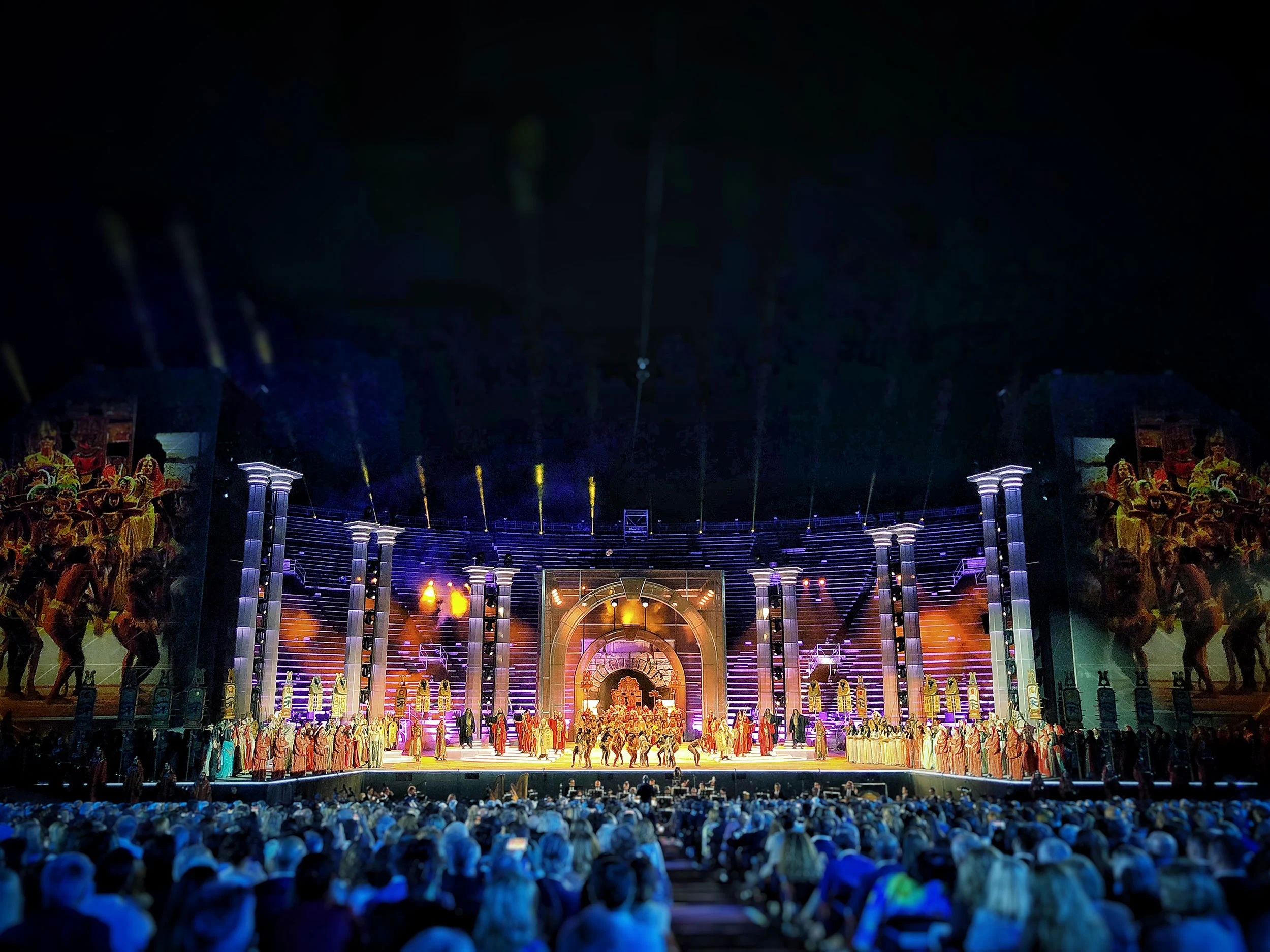Vista notturna del palco dell'Arena: colonne, arco centrale luminoso e un grande cast in costume schierato davanti al pubblico – La Notte di Andrea Bocelli all'Arena di Verona, Italia, 2018 – scenografia per concerti