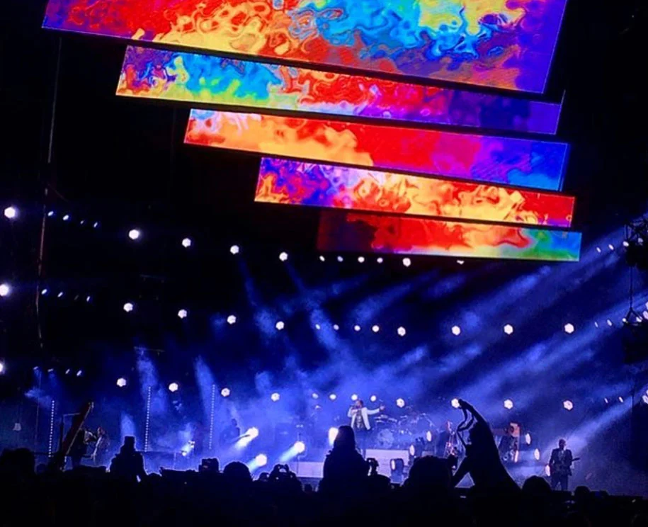 Barre video sovrapposte in colori vorticosi sopra la band, fasci bianchi che tagliano il fumo – Cesare Cremonini Stadi 2018, Italia – scenografia per concerti