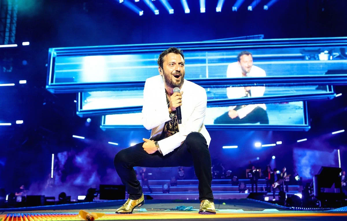 Cesare Cremonini accovacciato sul palco, la sua immagine su una pila di barre video blu alle sue spalle – Cesare Cremonini Stadi 2018, Italia – scenografia per concerti