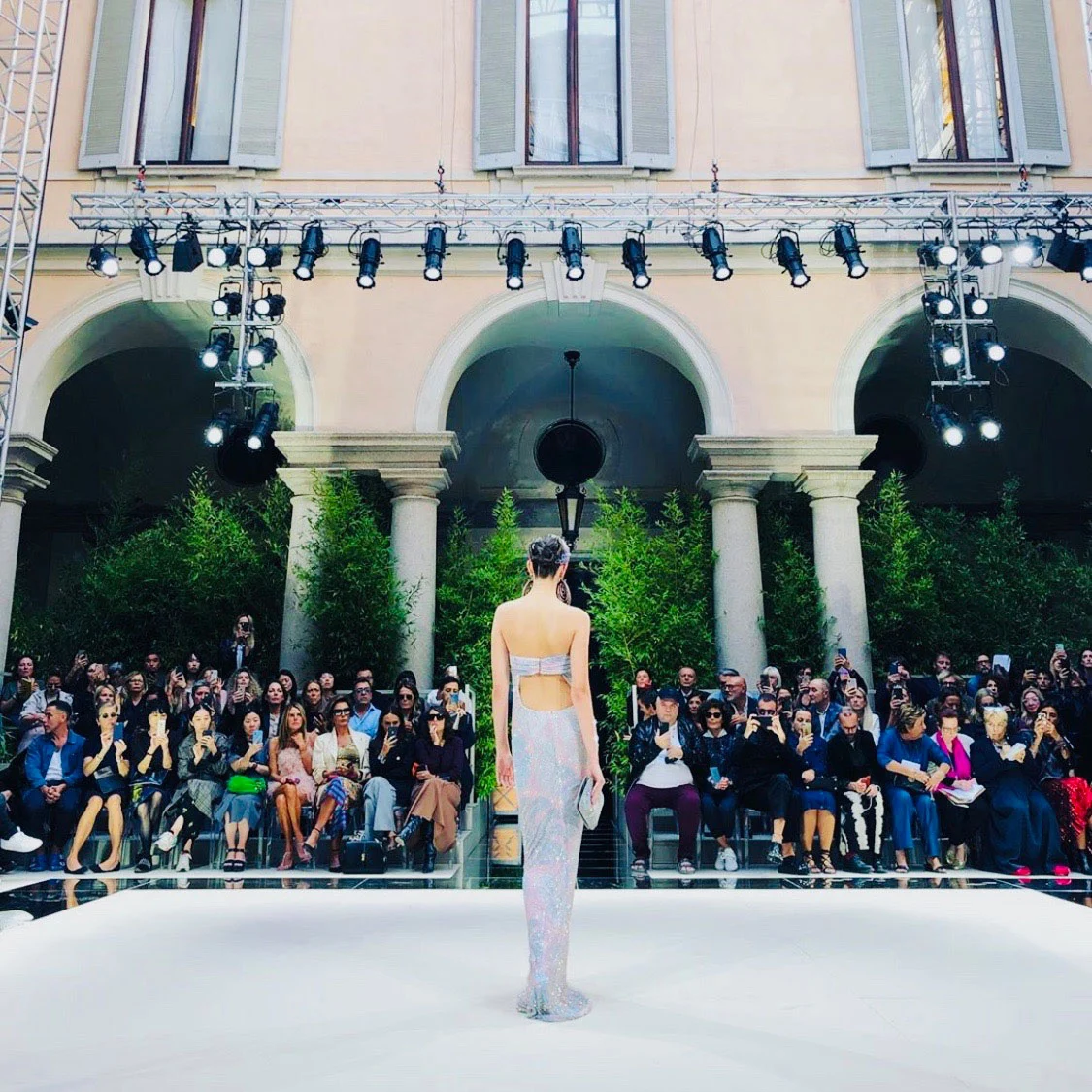 Modello sulla passerella bianca visto da dietro, di fronte agli ospiti seduti sotto il porticato e a una struttura luci – Giorgio Armani SS20 Uomo e Donna, Milano, Italia, 2019 – scenografia per sfilate