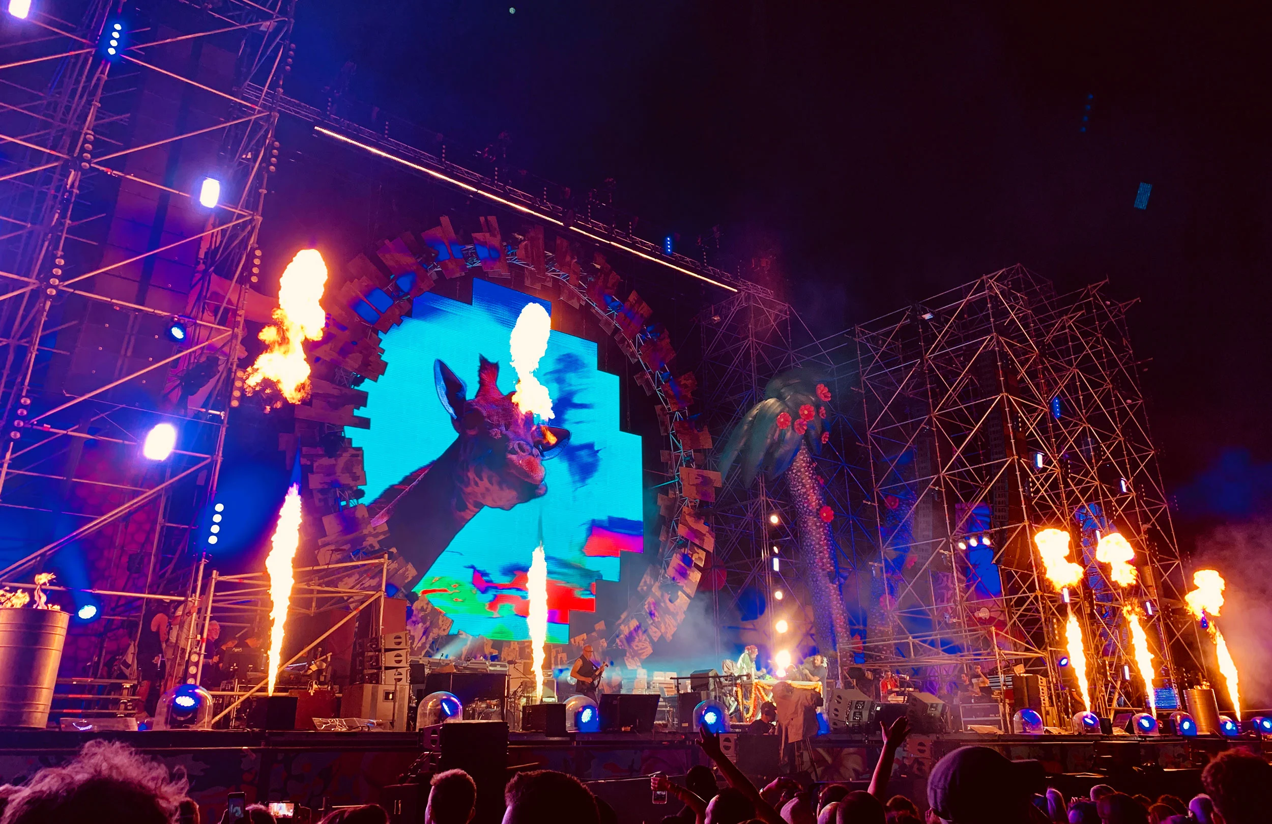 Spettacolo notturno con getti di fiamme davanti allo schermo ad anello e torri di tubi illuminate di blu – Jova Beach Party 2019, Italia – scenografia per concerti