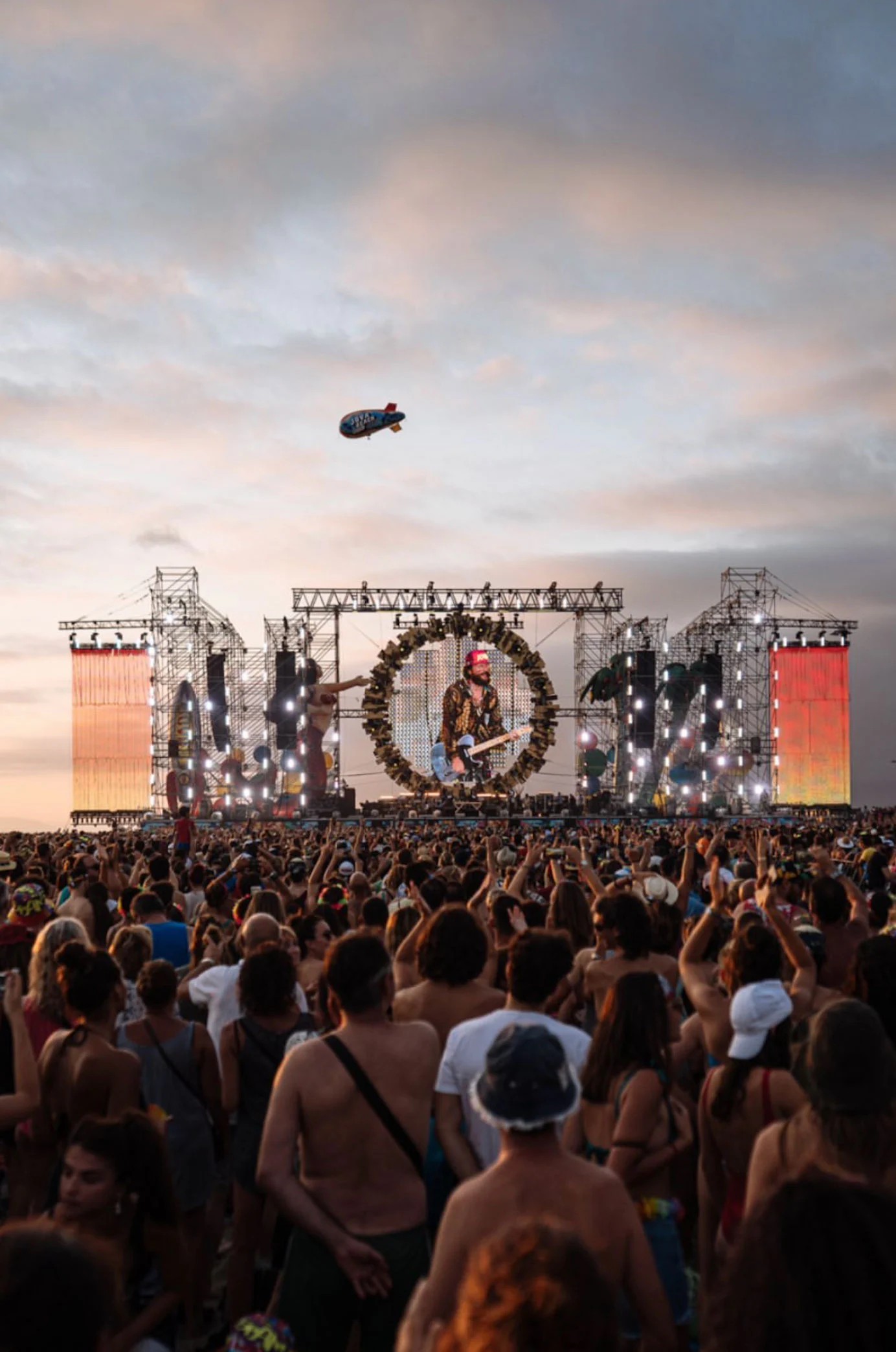 Pubblico al tramonto davanti al palco del Jova Beach, con un dirigibile in volo sopra i tubi – Jova Beach Party 2019, Italia – scenografia per concerti