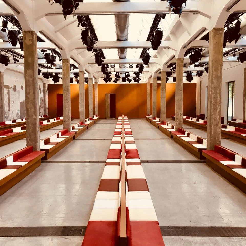 Location della sfilata Marni AW 2017: lunghe panche rosse e bianche tra pilastri di cemento, una parete arancione in fondo – Marni AW 2017, Milano, Italia – scenografia per sfilate