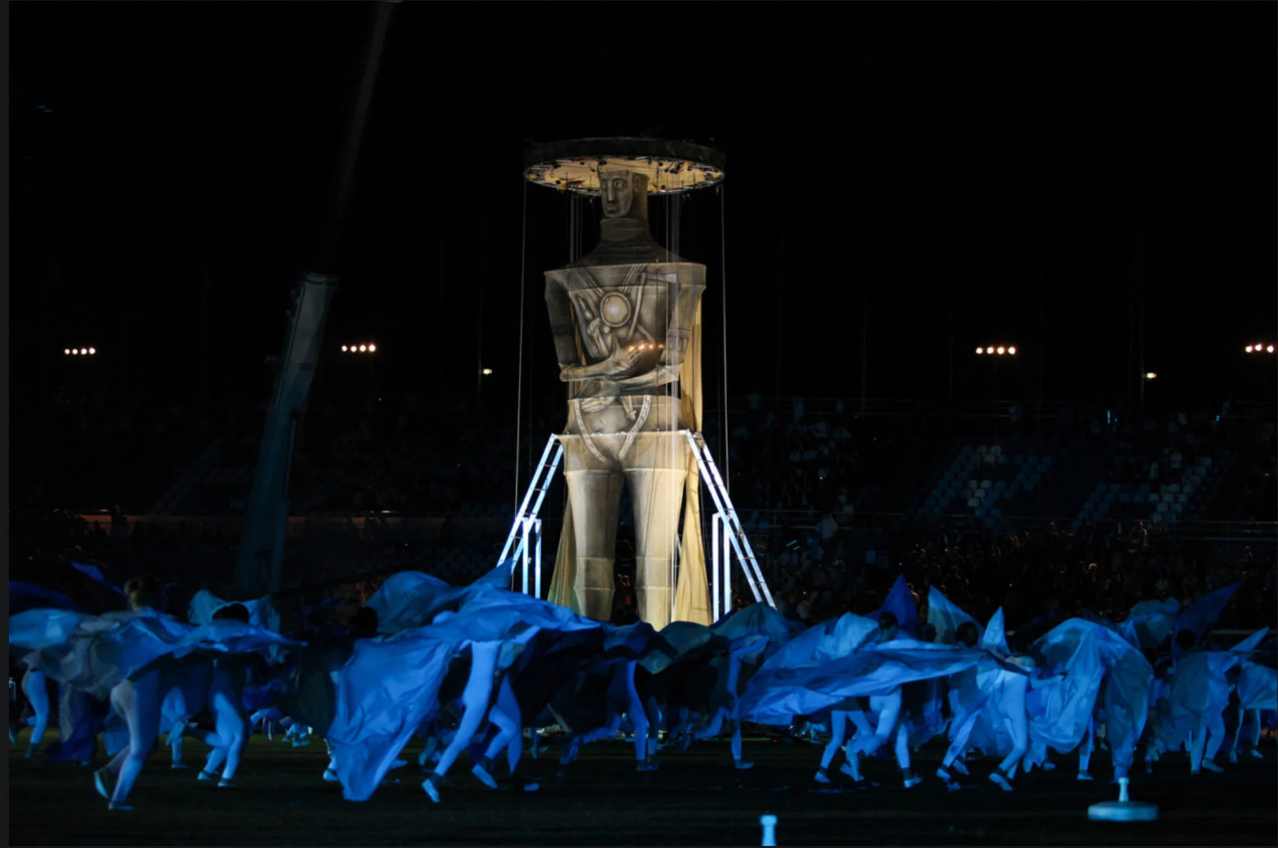 Enorme figura illuminata su una struttura sopra artisti che agitano tessuti blu nello stadio – Cerimonia di apertura dei Giochi del Mediterraneo Pescara 2009, Italia, 2019 – progettazione di eventi