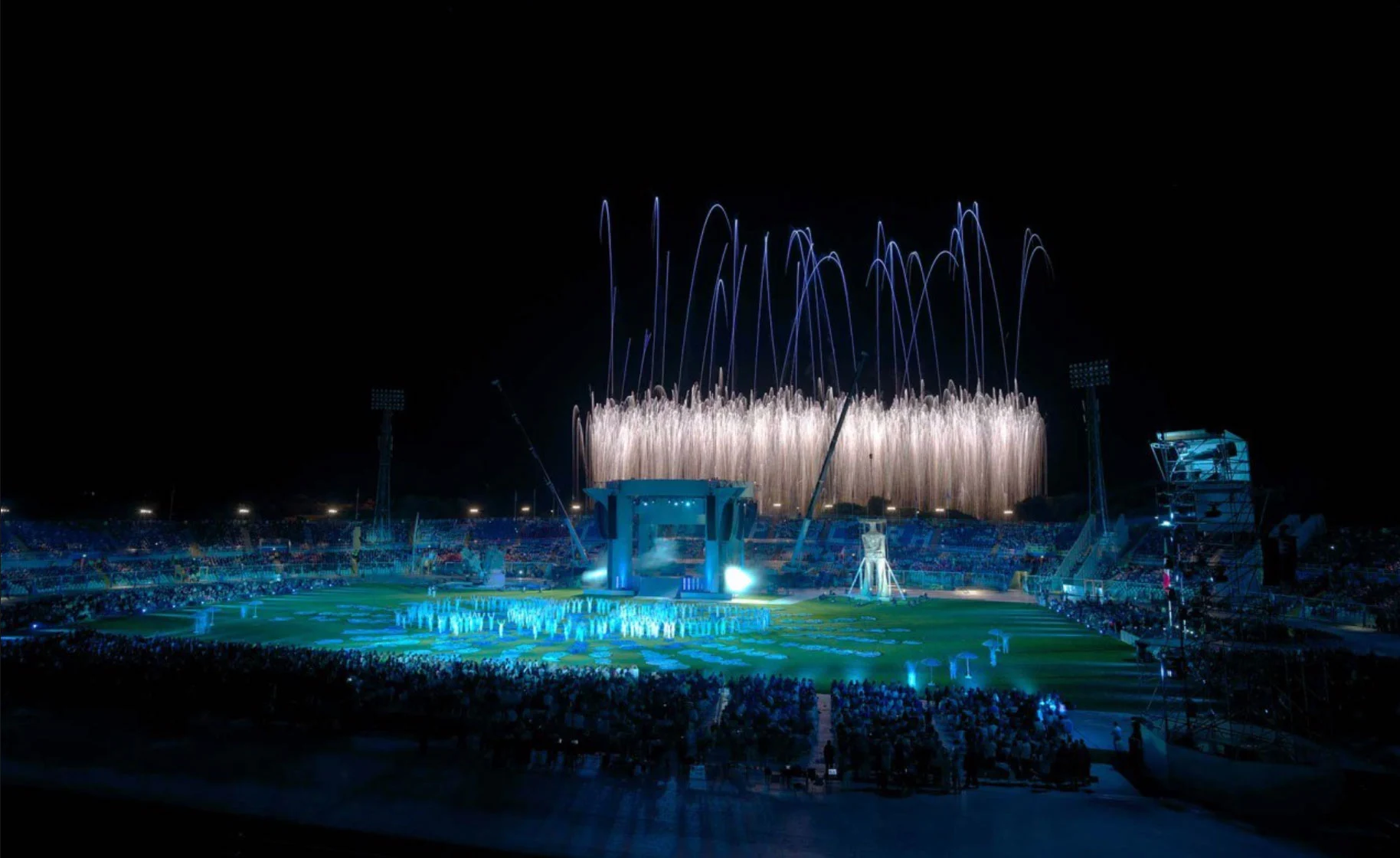 Vista notturna dello stadio con fontane pirotecniche sopra un campo illuminato di blu e il pubblico – Cerimonia di apertura dei Giochi del Mediterraneo Pescara 2009, Italia, 2019 – progettazione di eventi