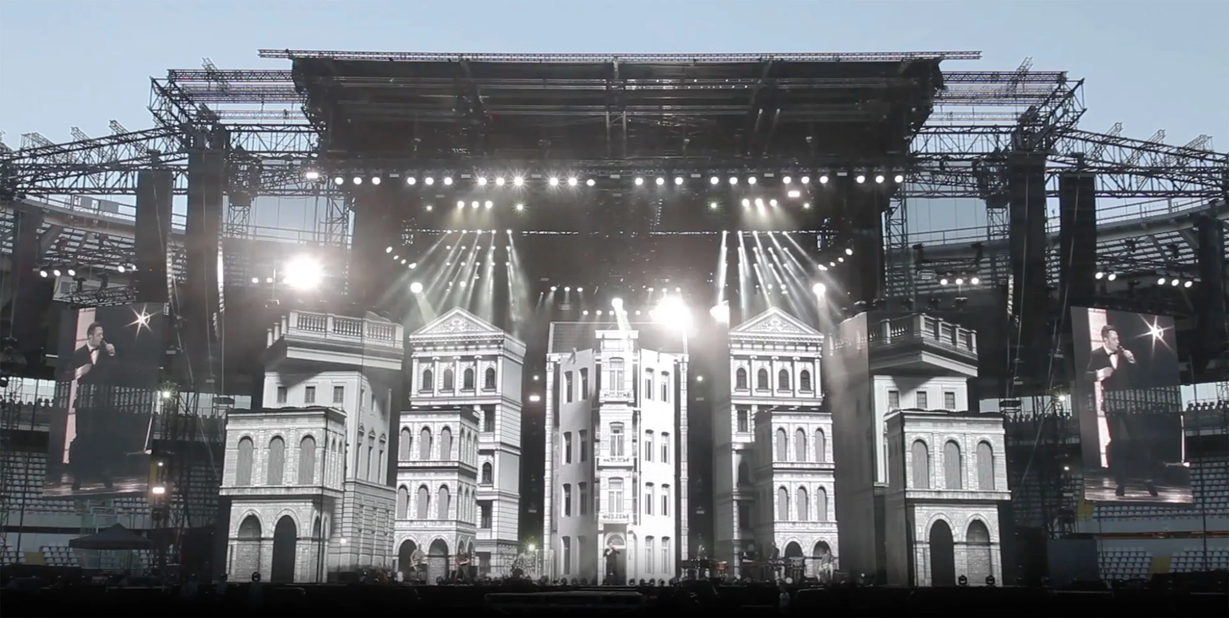 Scenografia del palco negli stadi costruita come facciate classiche bianche, con riflettori e schermi laterali al crepuscolo – Tiziano Ferro Lo Stadio Tour 2015, Italia – scenografia per concerti