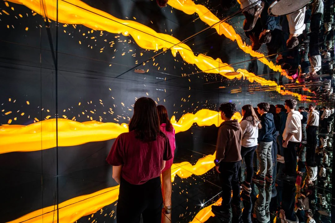 Visitatori in una stanza a specchio circondata da schermi con flussi di luce gialla – STEP FuturAbility District by Fastweb, Milano, Italia, 2022 – allestimento espositivo