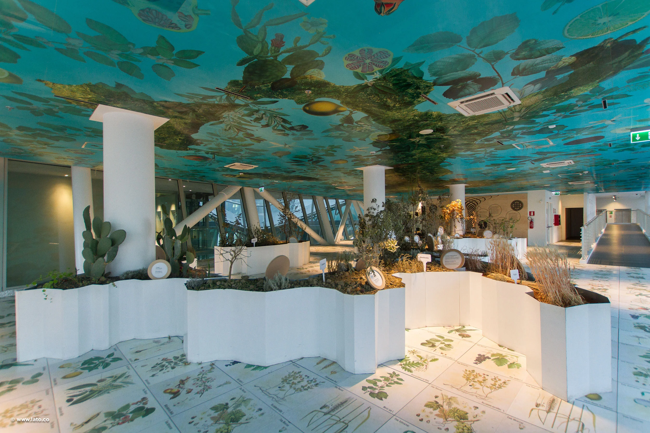 Sala con soffitto dipinto a fogliame, fioriere bianche ondulate con piante e piastrelle botaniche a pavimento – Padiglione Italia all'Expo 2015, Milano, Italia – allestimento espositivo