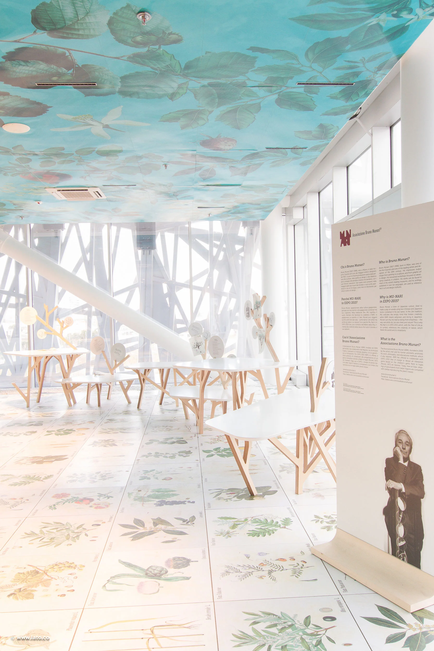Sala espositiva con un murale botanico a soffitto, piastrelle illustrate con piante e tavoli in legno a forma di albero – Padiglione Italia all'Expo 2015, Milano, Italia – allestimento espositivo