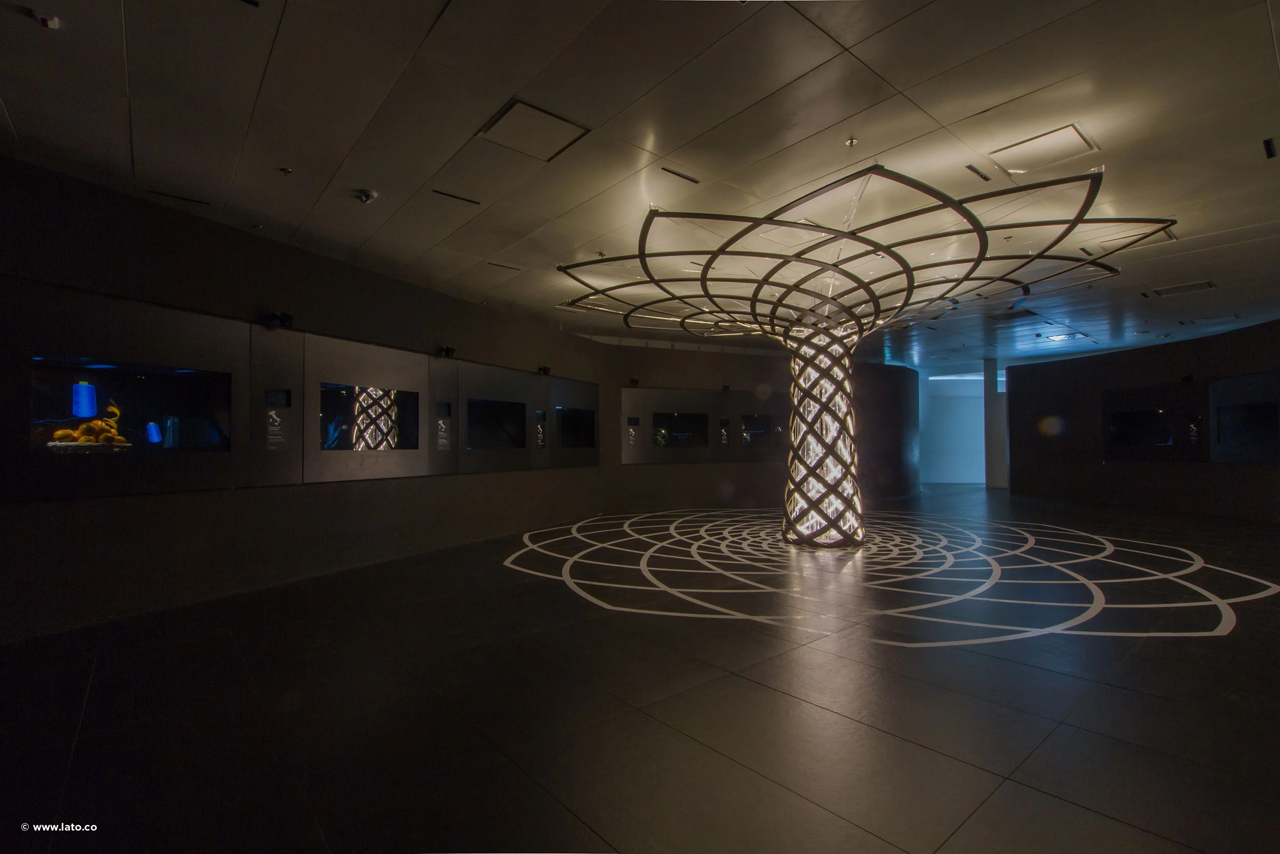 Sala espositiva buia con una colonna a reticolo retroilluminata a forma di Albero della Vita e il suo profilo proiettato – Padiglione Italia all'Expo 2015, Milano, Italia – allestimento espositivo