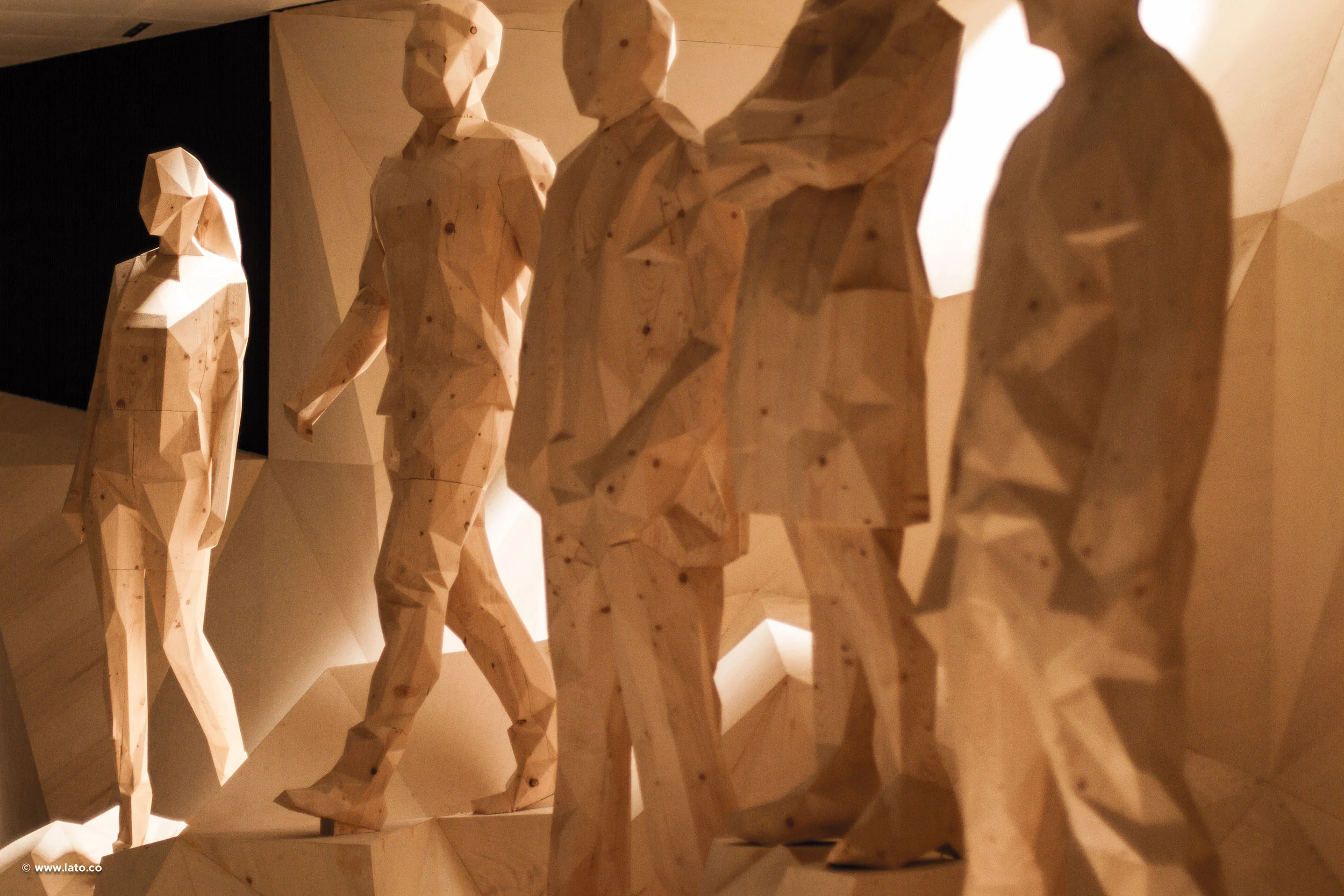 Figure sfaccettate in legno di persone che camminano su un paesaggio scolpito in legno, illuminate di lato da luce calda – Padiglione Italia all'Expo 2015, Milano, Italia – allestimento espositivo