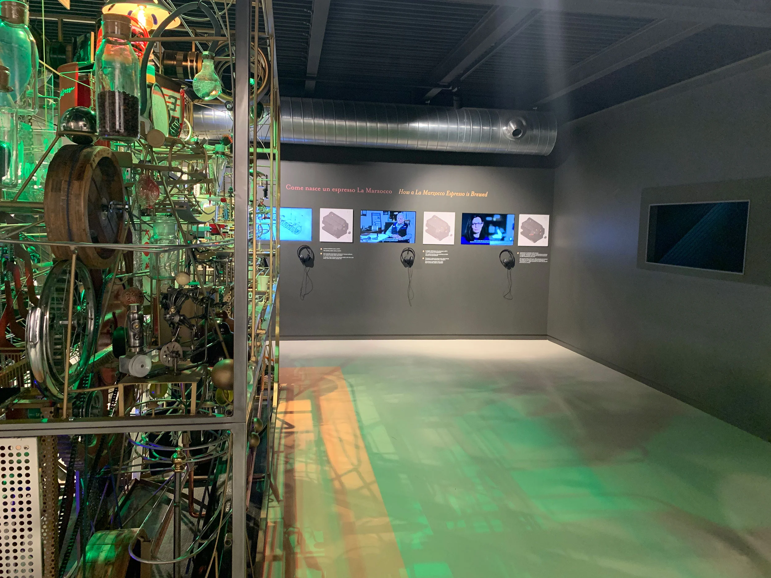 Sala espositiva buia con una scultura-macchina cinetica, schermi video e cuffie alla parete – La Marzocco Accademia del Caffè Espresso, Firenze, Italia, 2018 – interior design