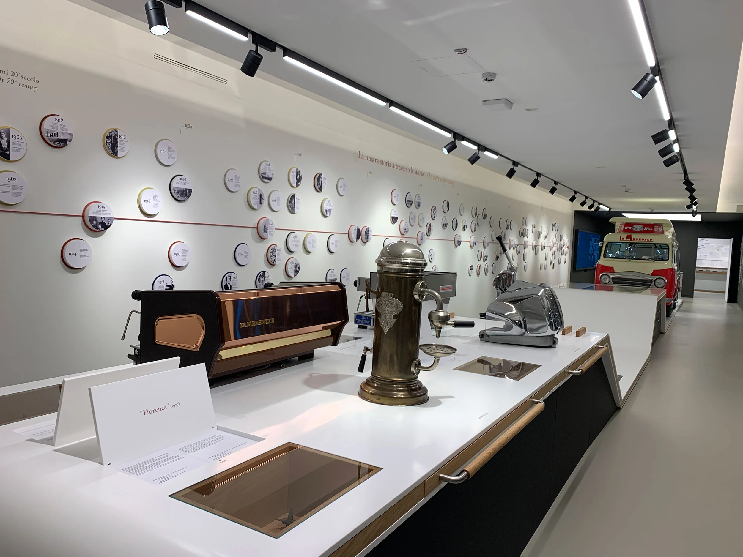 Bancone del museo con macchine per espresso storiche, una cronologia di foto rotonde e un furgone d'epoca – La Marzocco Accademia del Caffè Espresso, Firenze, Italia, 2018 – interior design