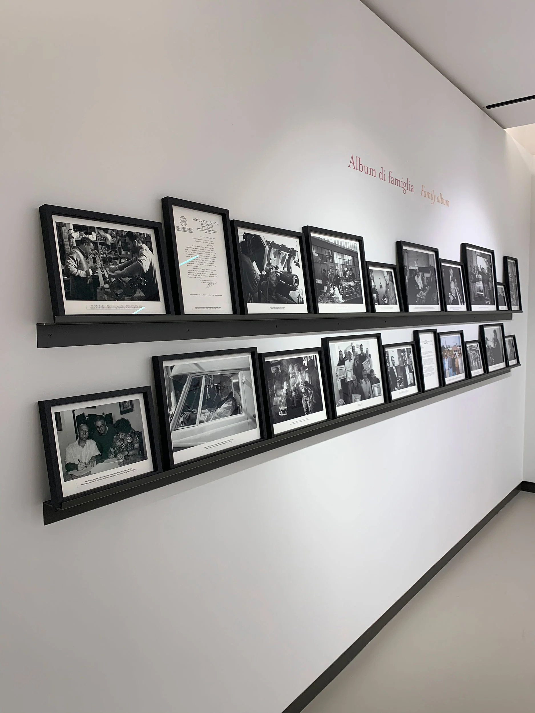 Parete di corridoio con due mensole di foto in bianco e nero incorniciate sotto il titolo Album di famiglia – La Marzocco Accademia del Caffè Espresso, Firenze, Italia, 2018 – interior design