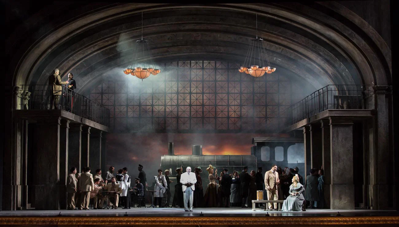 Scenografia di una stazione ferroviaria con copertura a volta in ferro e vetro e una locomotiva a vapore, il coro riunito sul palco – Manon Lescaut al Teatro San Carlo, Napoli, Italia, 2022 – scenografia d'opera