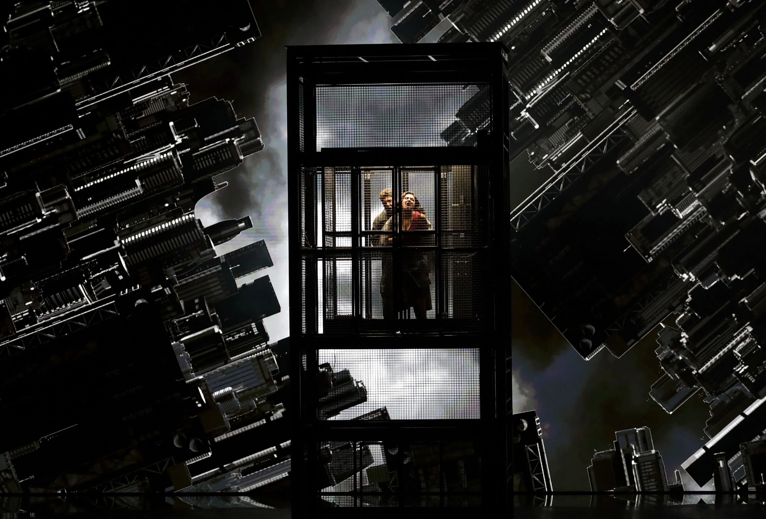 Due cantanti in una cabina d'ascensore in vetro tra proiezioni di grattacieli capovolti – Macbeth al Teatro alla Scala, Milano, Italia, 2021 – scenografia d'opera
