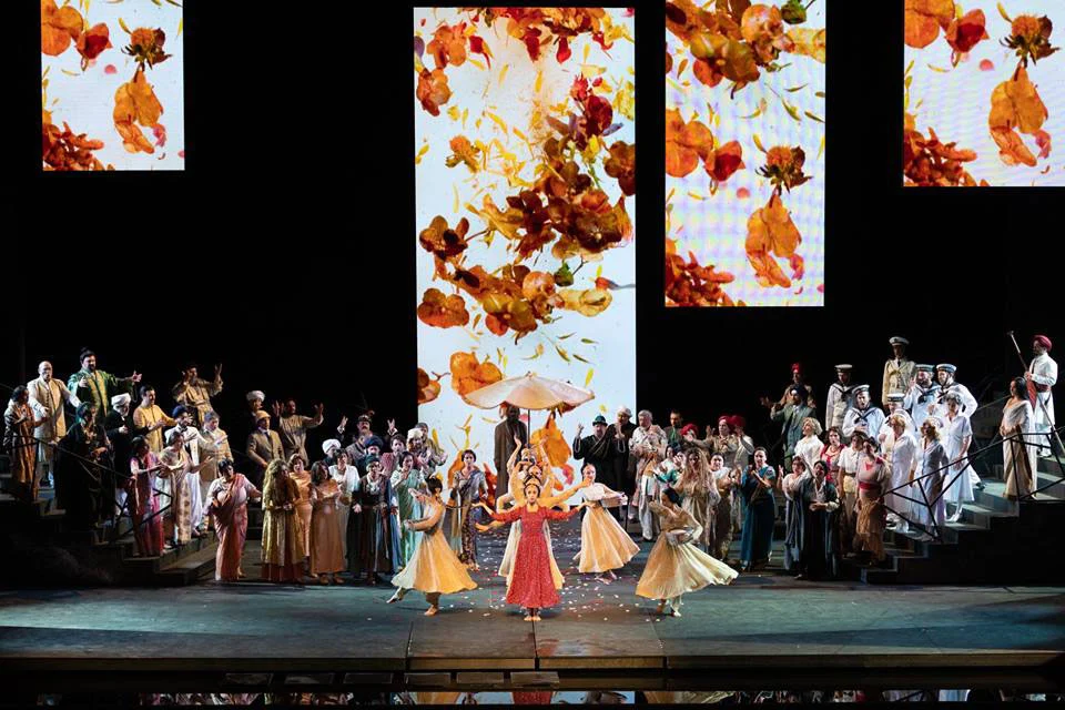 Scena di Lakmé con tutto il coro sulle scale, danzatori in giallo e rosso e schermi di foglie autunnali che cadono – Lakmé alla Royal Opera House Muscat, Oman, 2019 – scenografia d'opera