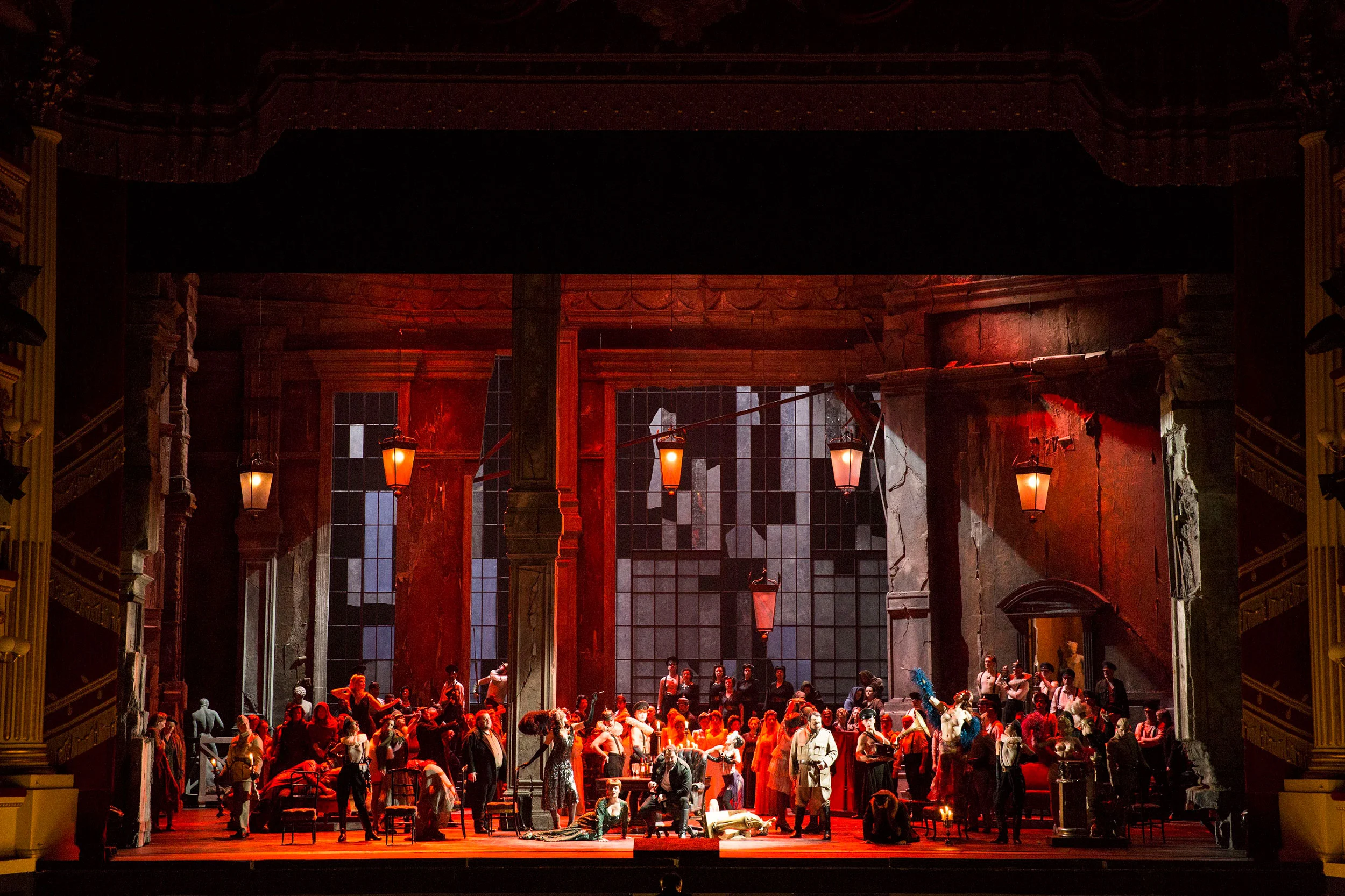 Scena di banchetto affollata in luce rossa nel palazzo in rovina, con lanterne appese in alto – Attila al Teatro alla Scala, Milano, Italia, 2018 – scenografia d'opera