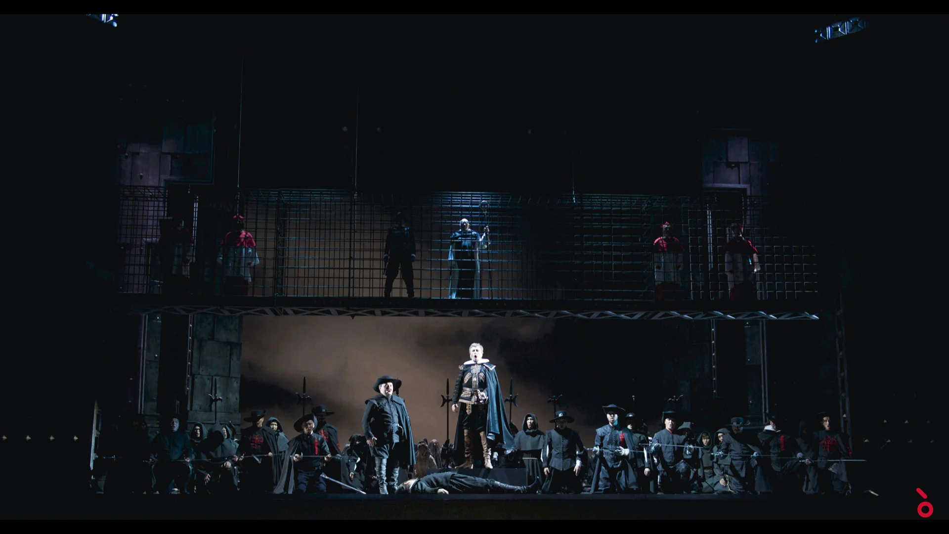 Figure di soldati sotto una scenografia di gabbie di ferro su due livelli, un uomo disteso sul palco davanti – Don Carlo all'Astana Opera, Kazakistan, 2023 – scenografia d'opera