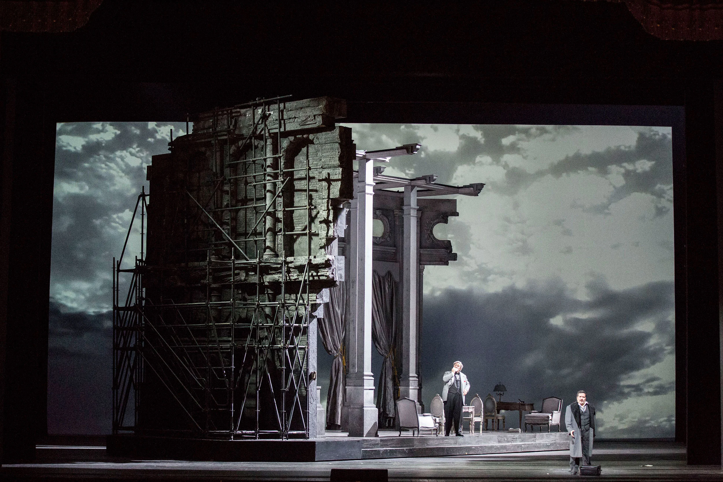 Rovina con ponteggi e colonne su un palco girevole davanti a un fondale grigio nuvoloso, due cantanti – Don Pasquale al Teatro alla Scala, Milano, Italia, 2018 – scenografia d'opera